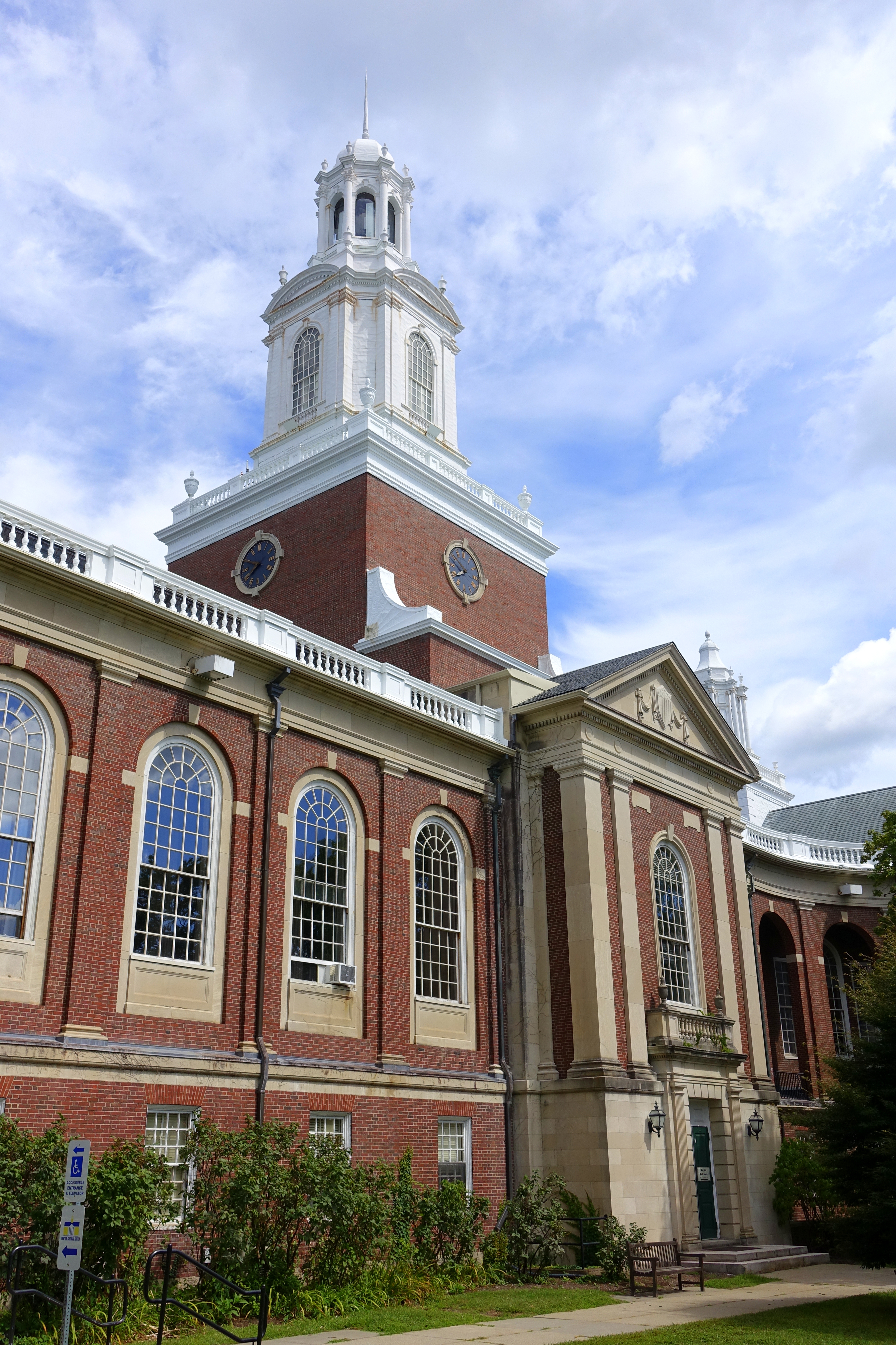 Red-brick building with white cupola clock tower and arched windows against a partly cloudy sky.