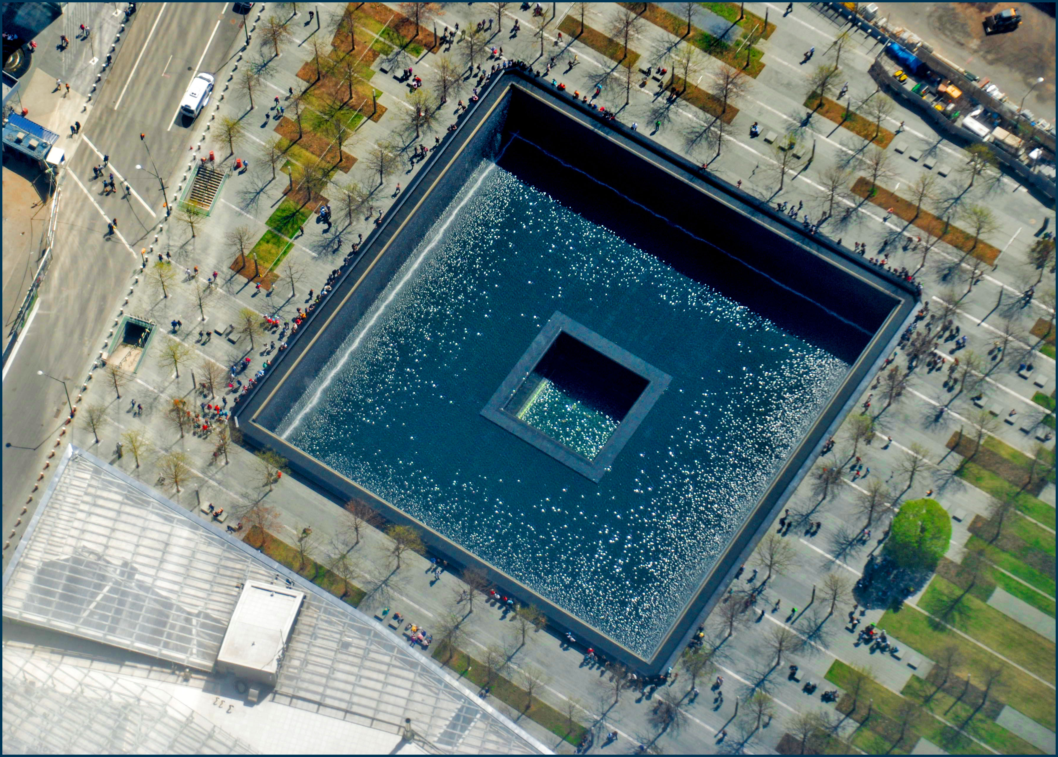 Aerial view of a large square reflecting pool surrounded by trees and pedestrians.