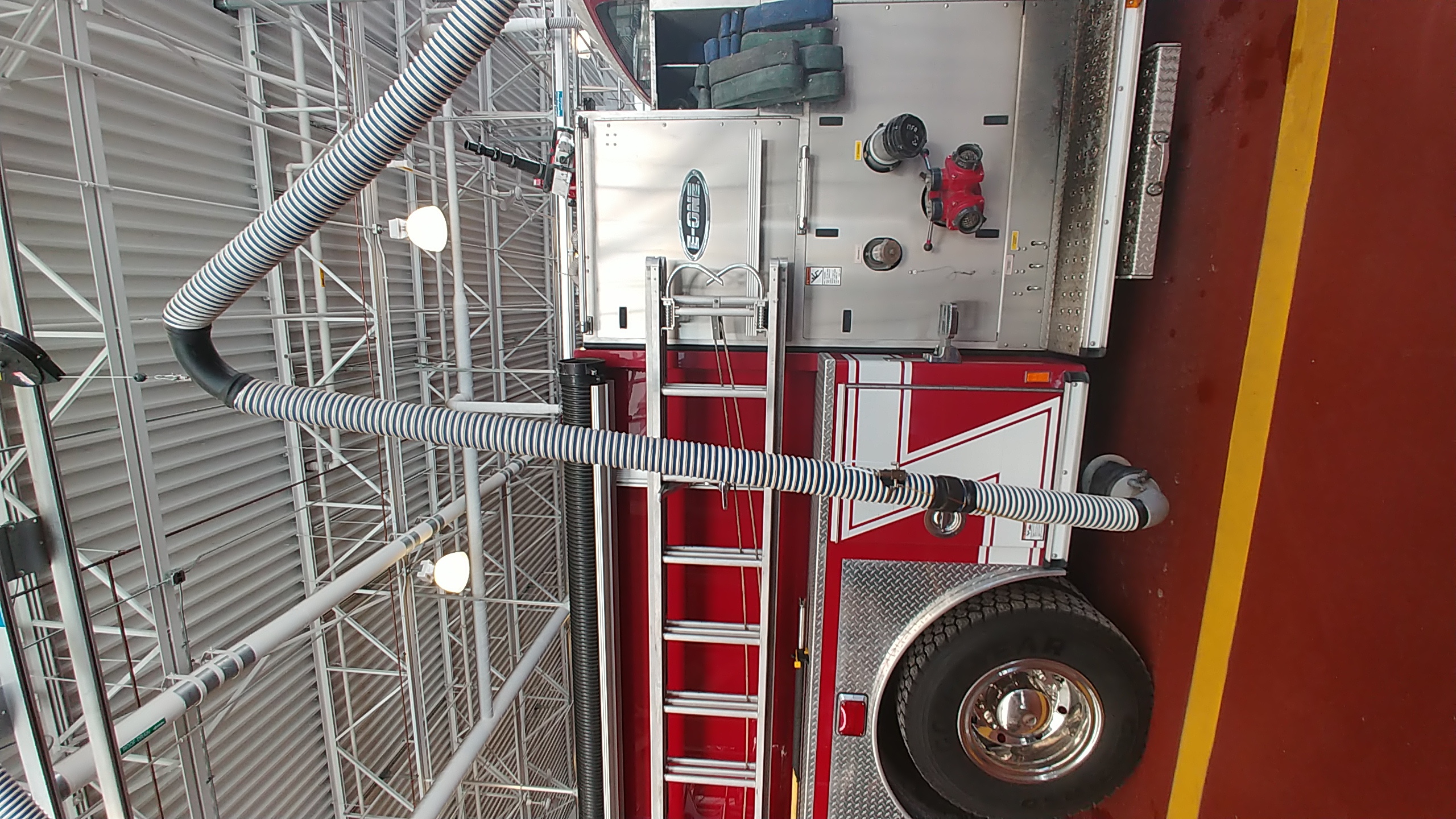 Red fire engine parked inside a fire station bay with an exhaust hose attached.