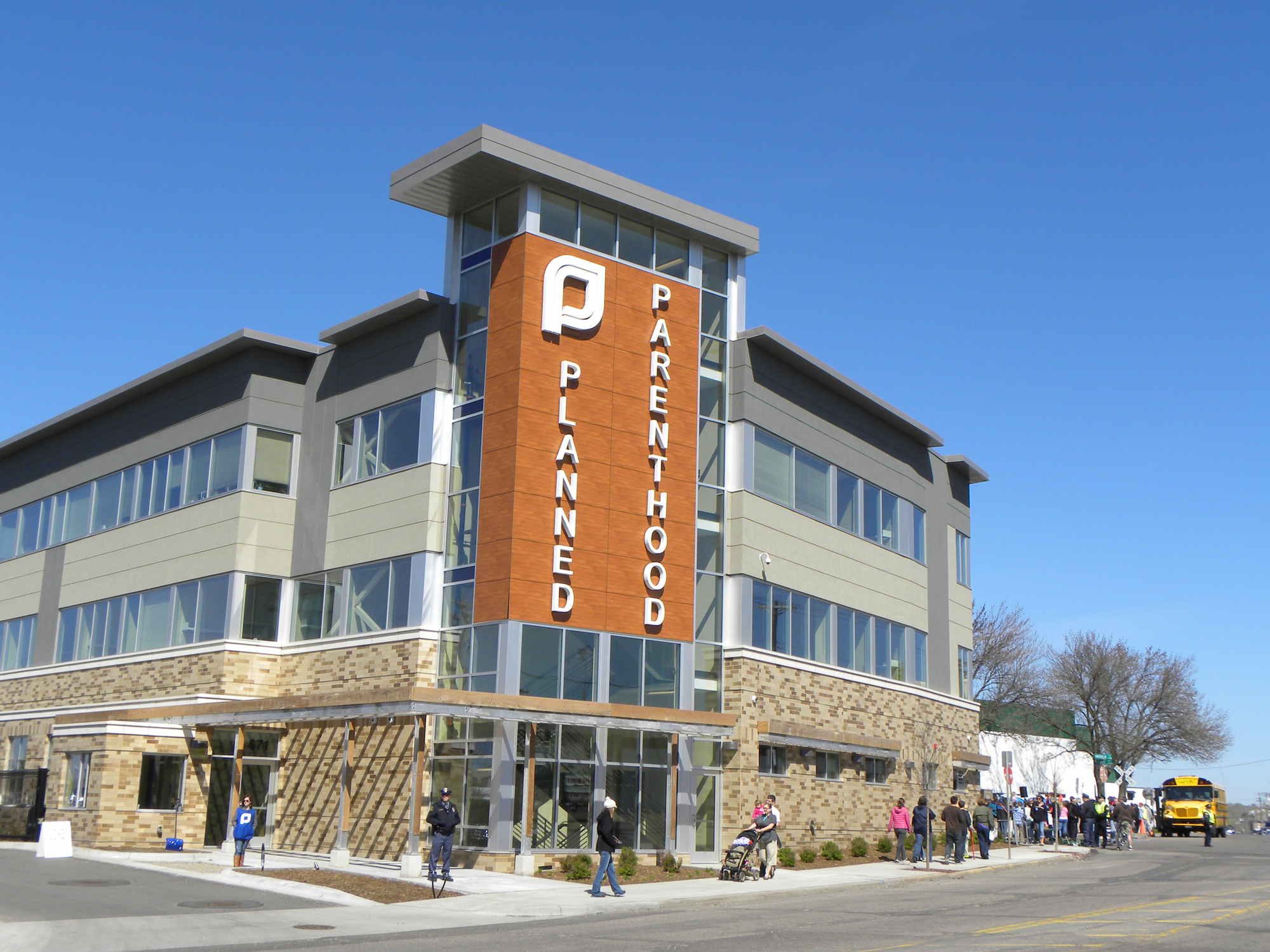 Multi-story Planned Parenthood building with signage and people on the sidewalk outside.