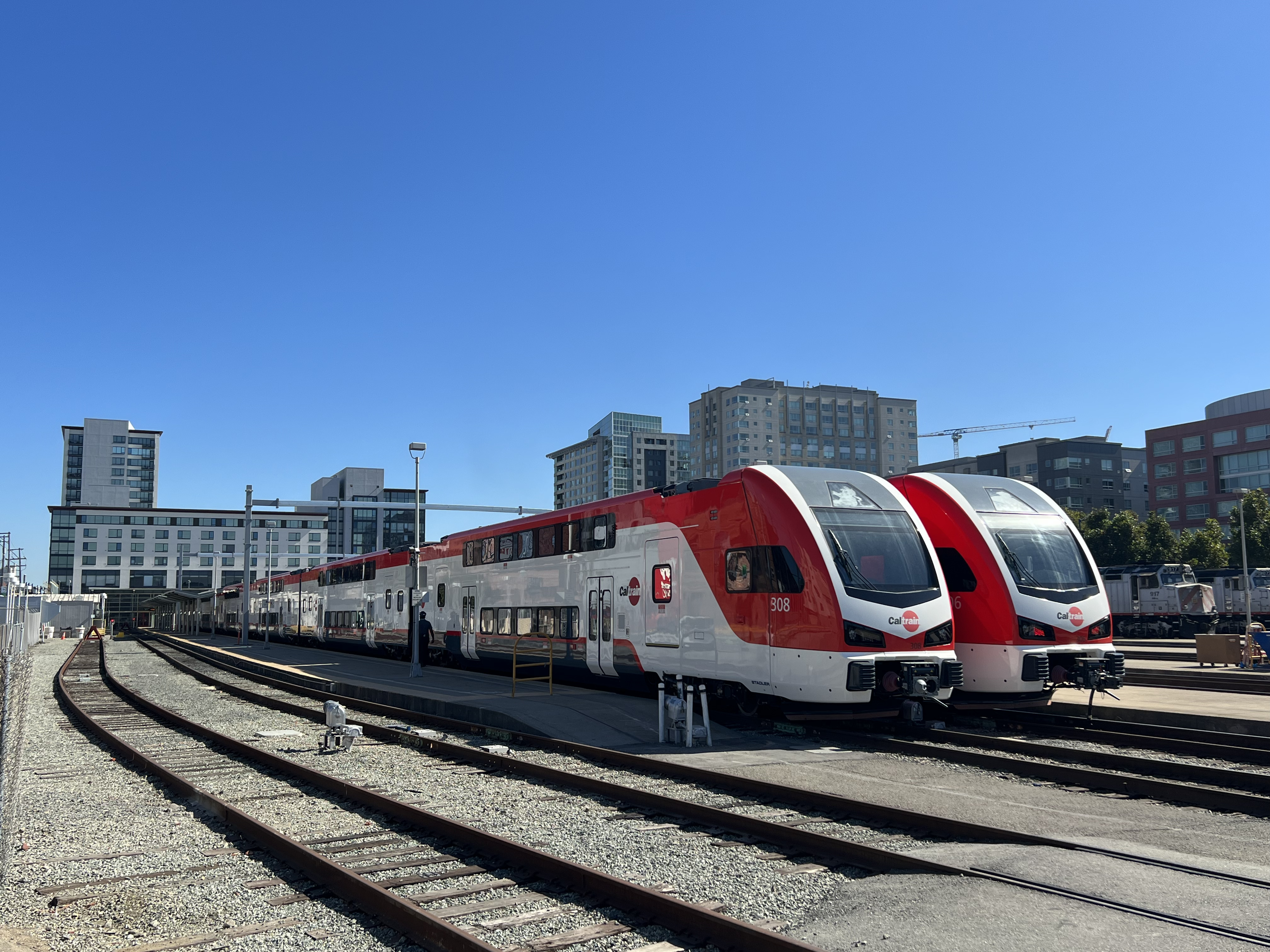 Two red and white Caltrain electric trains parked at a rail yard under blue skies.