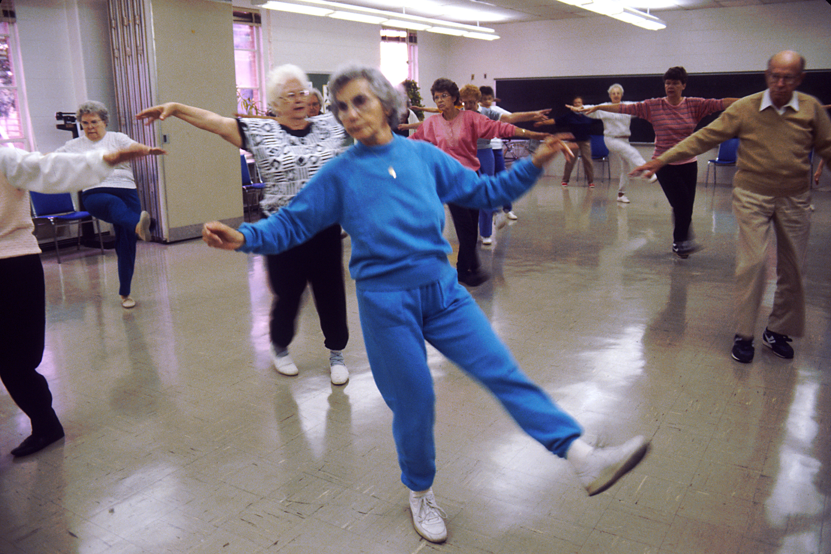 A group of older adults stretching their arms out during an indoor aerobics class.