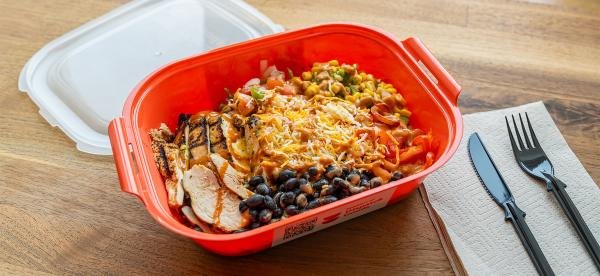A chicken bowl with beans, corn, and cheese in a bright red reusable container.