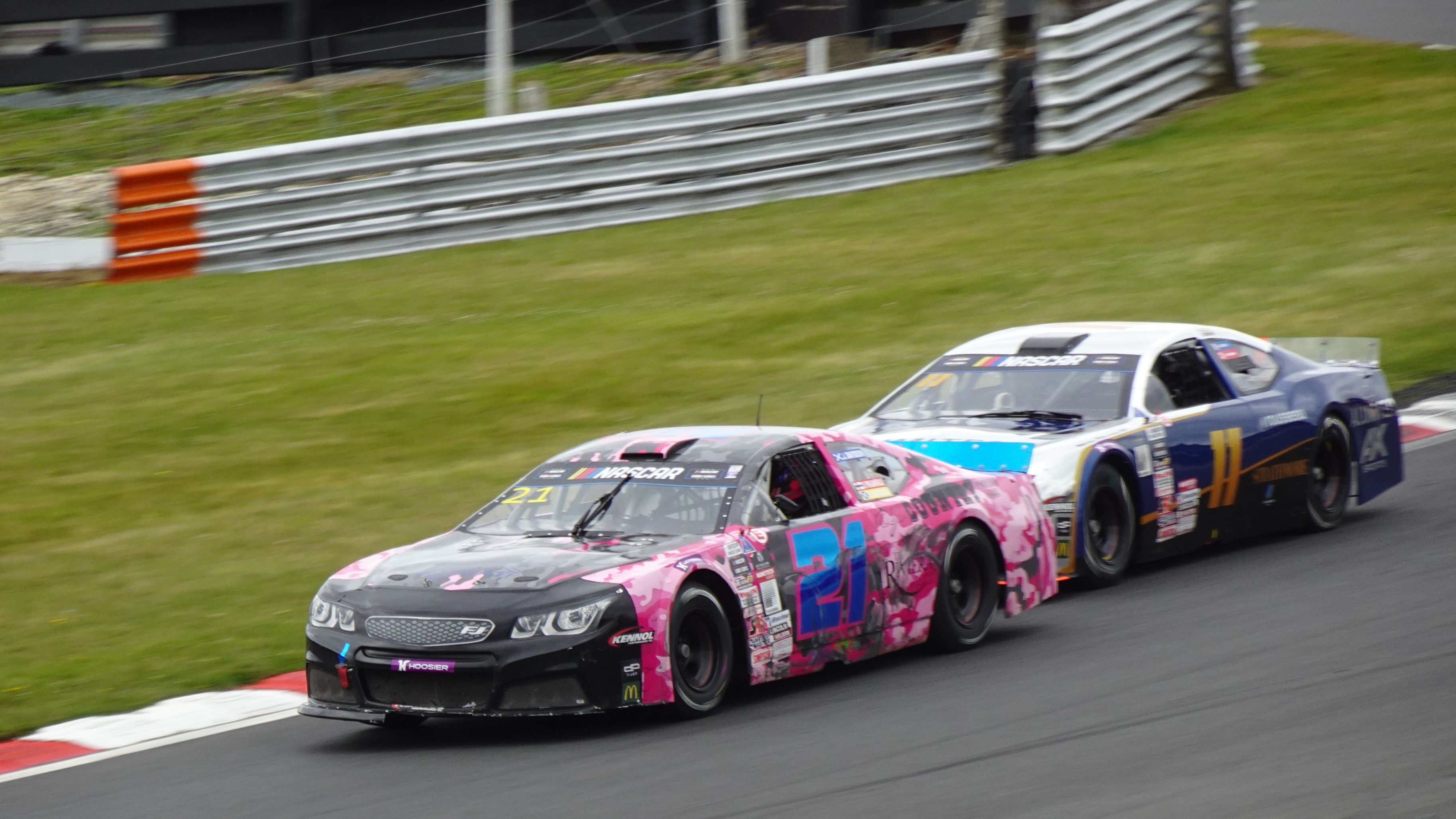 Two NASCAR stock cars race side by side on a road course circuit.