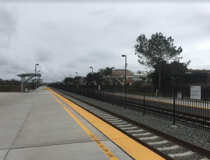 Commuter rail platform with yellow edge stripe, iron fencing, and a single track.