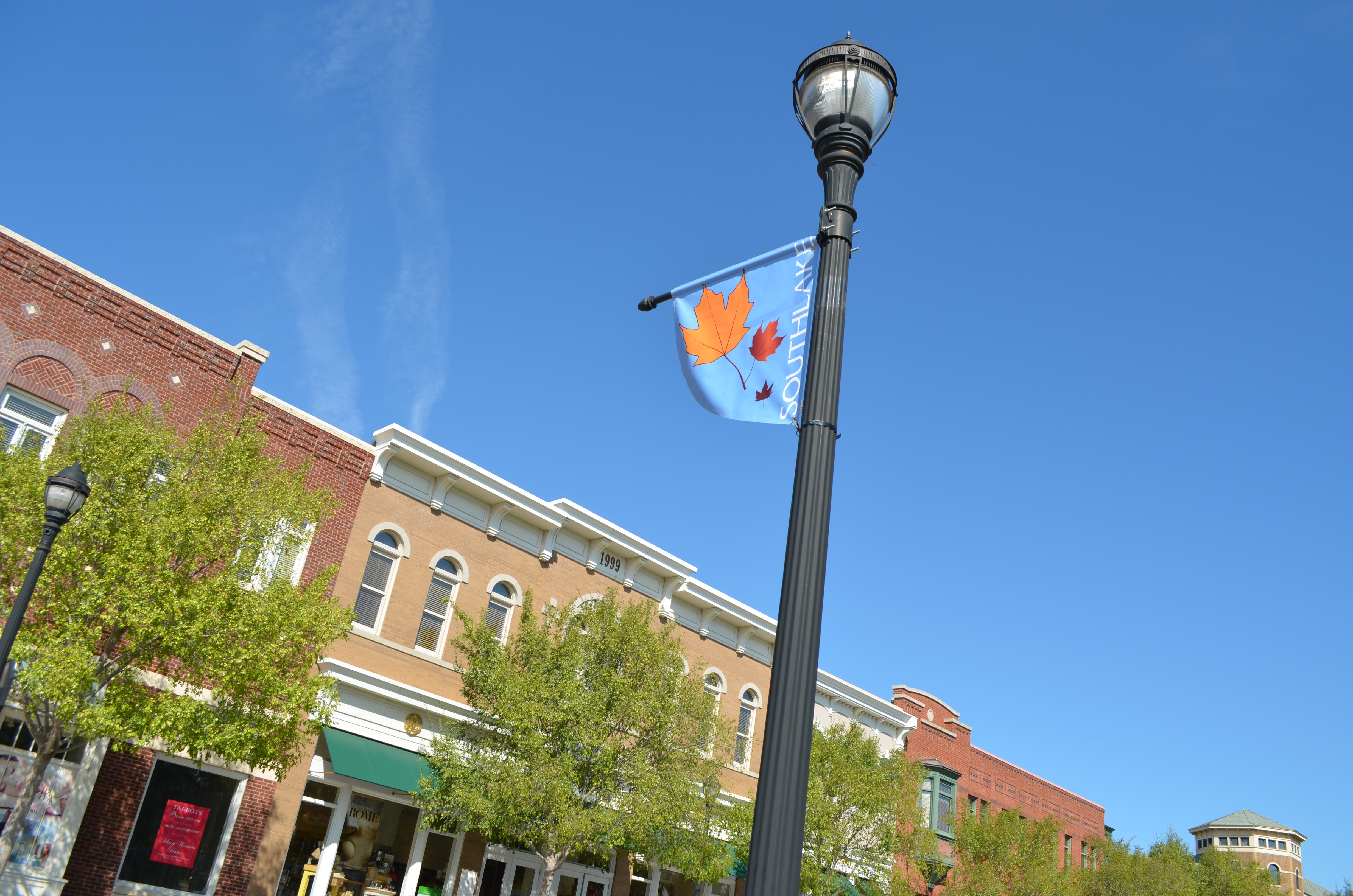 Decorative black street lamp and brick buildings lining a sunny Southlake Town Square street.