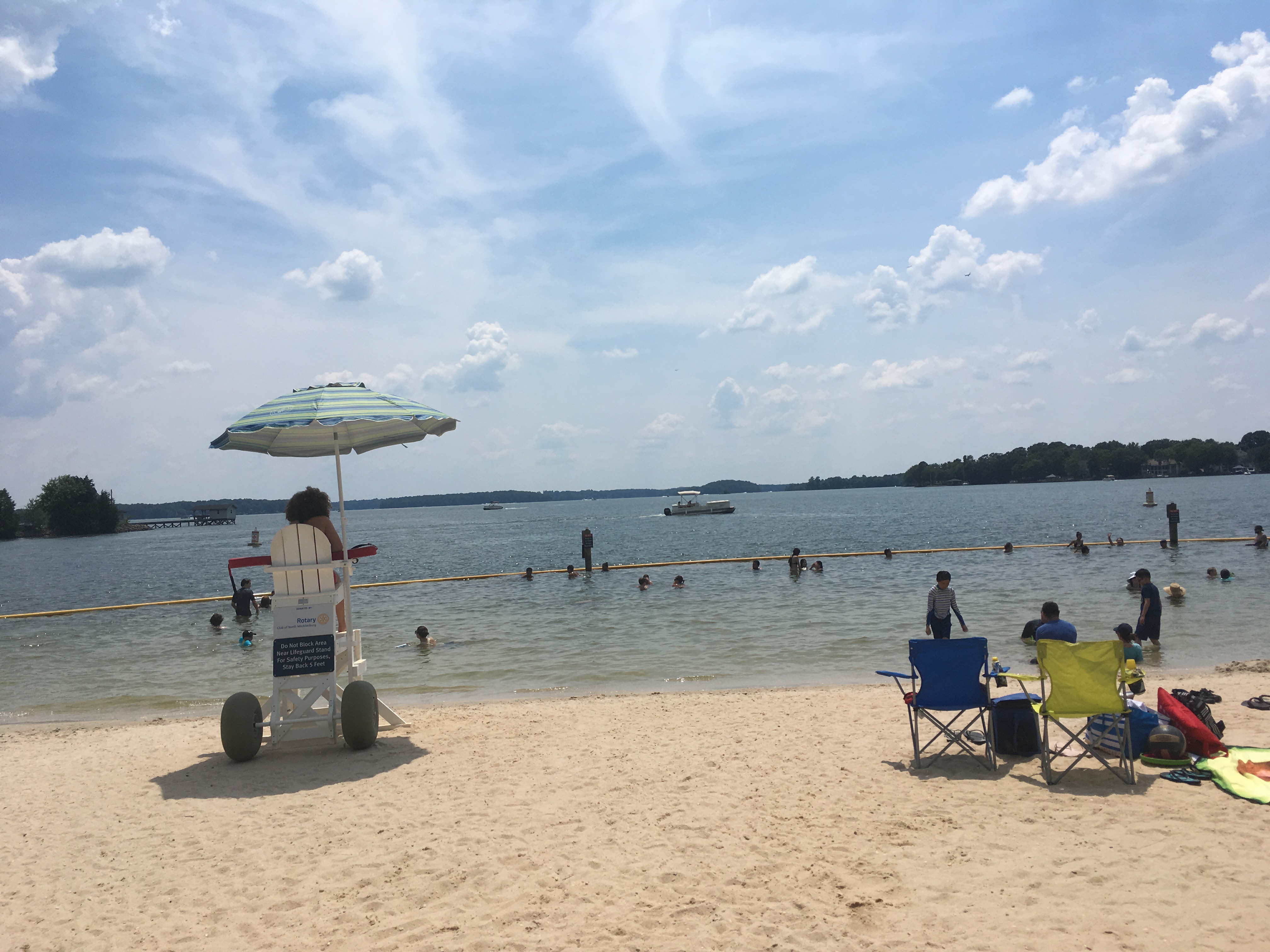 Sandy beach on Lake Norman with swimmers, a lifeguard stand, and a yellow swim boundary rope.
