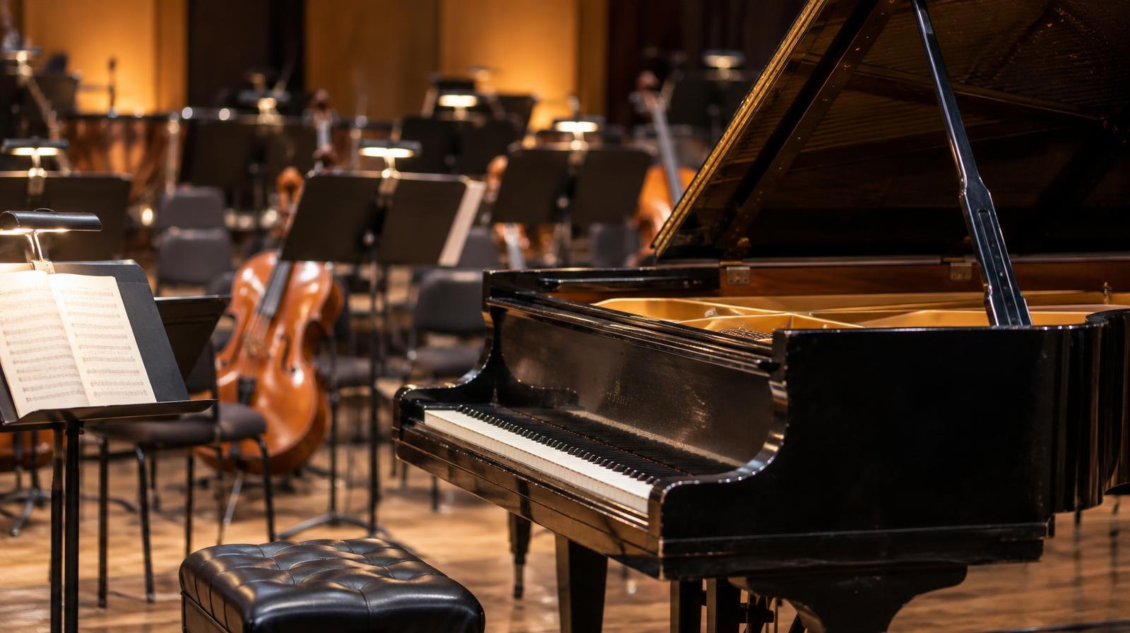 A grand piano on a concert stage surrounded by music stands under warm stage lighting.