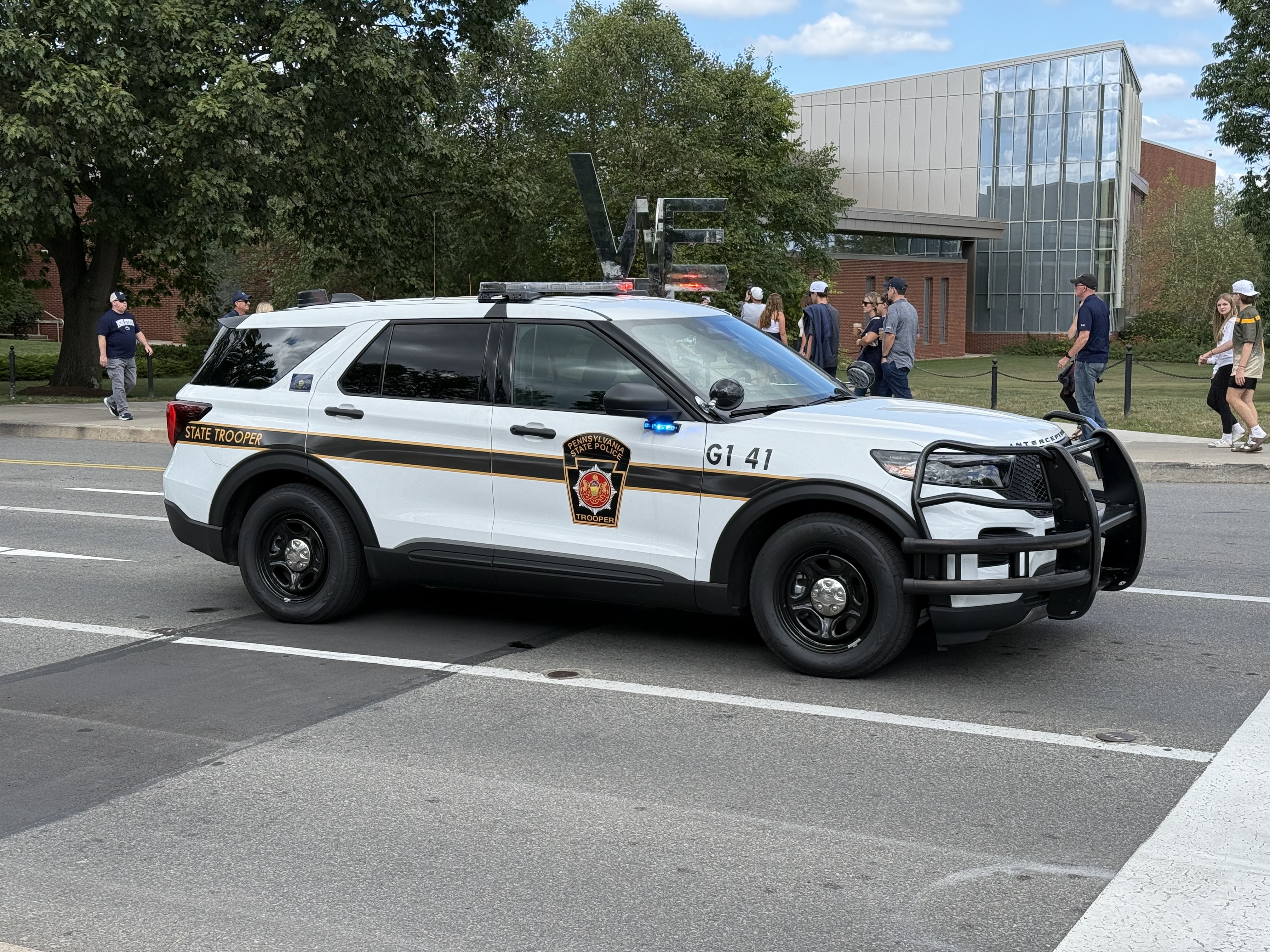 A white police SUV with a light bar parked on a road near a building.
