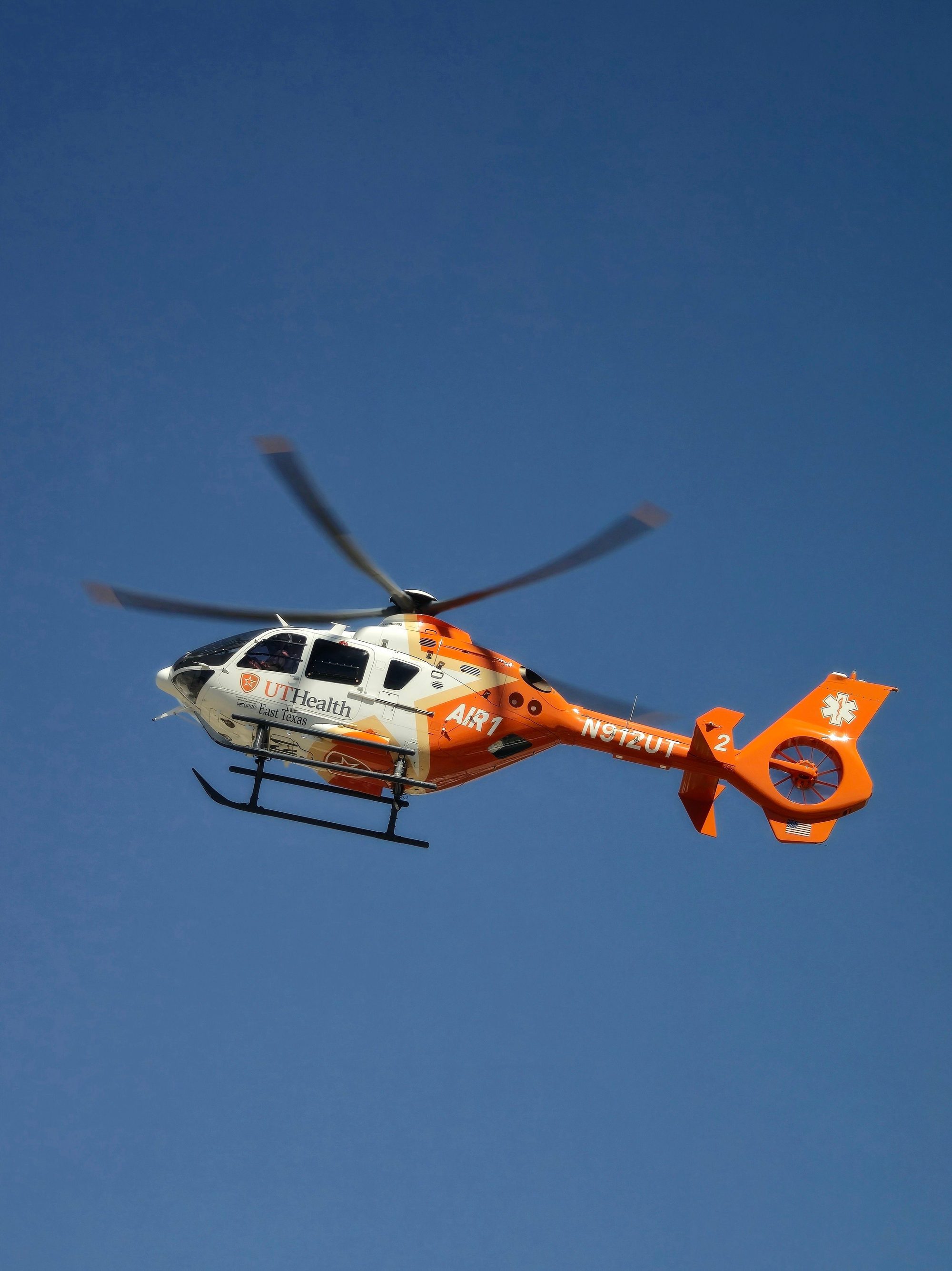 Orange and white medical helicopter flying against a clear blue sky.