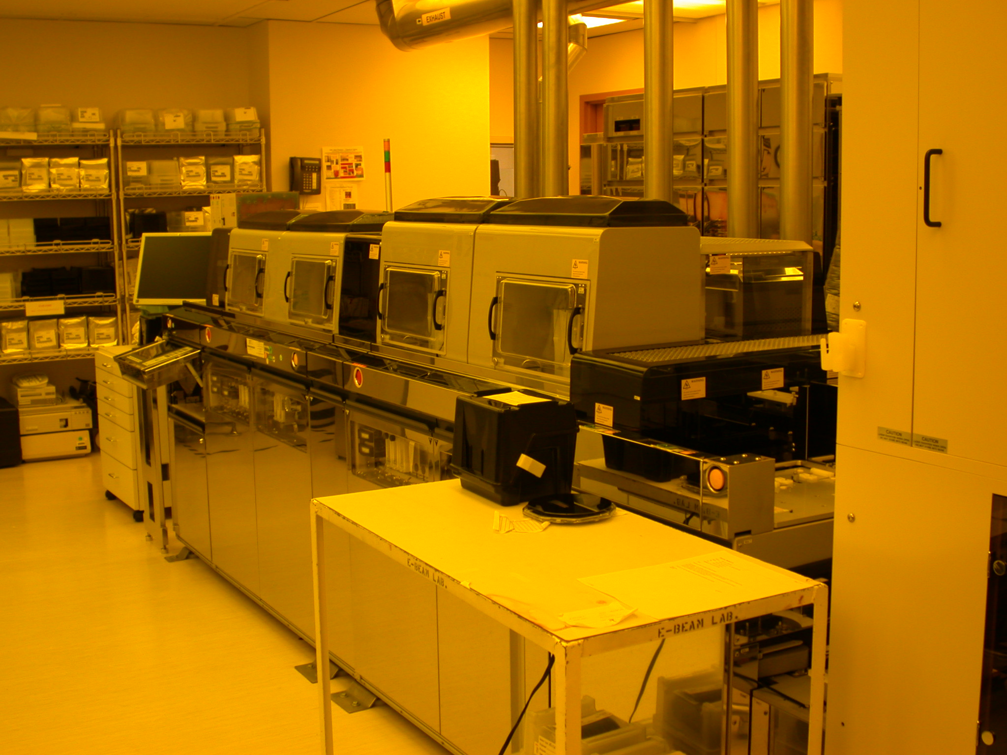 Amber-lit semiconductor cleanroom with rows of automated wafer processing machines.