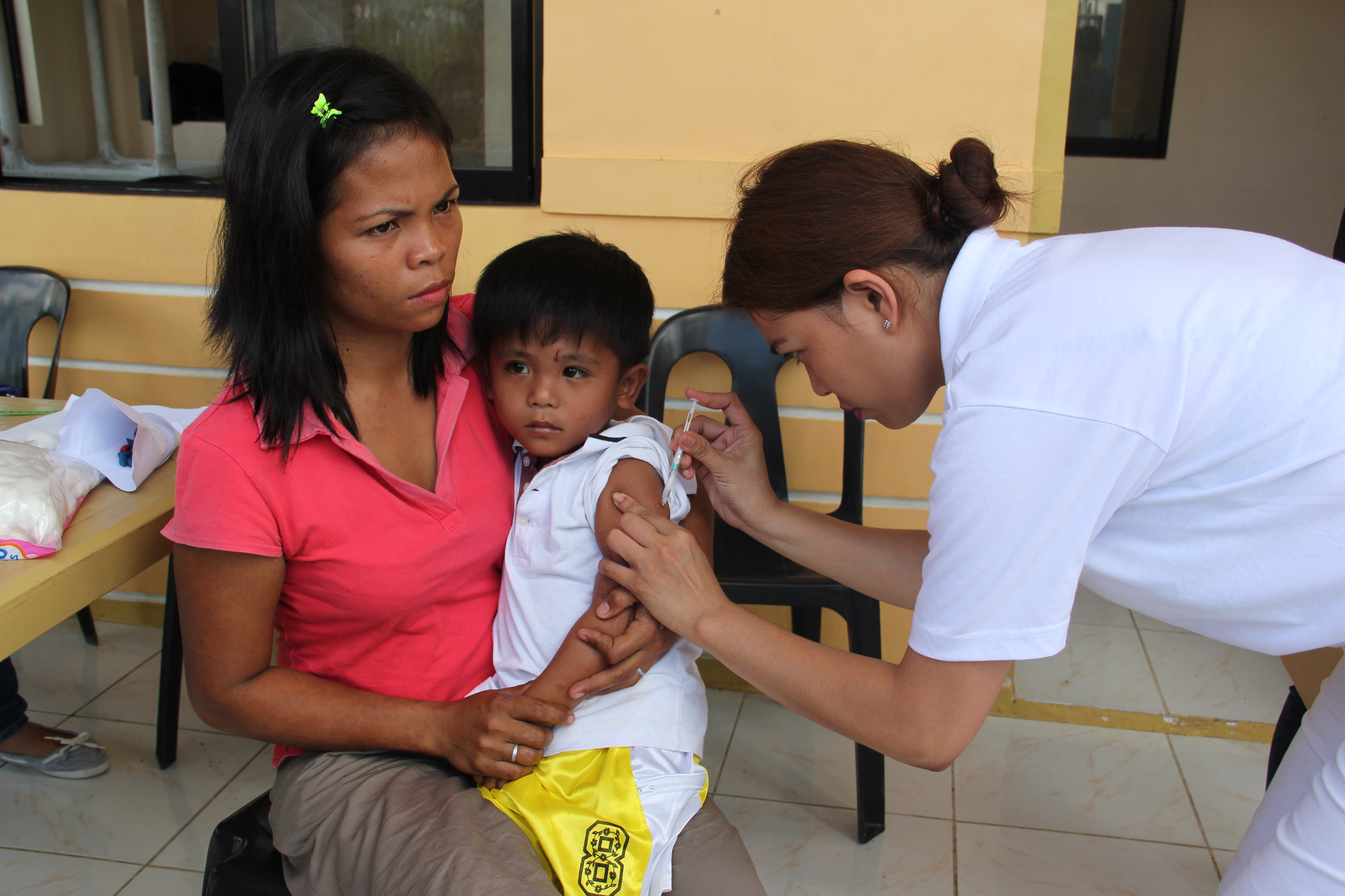 A young child receives an injection in the upper arm from a healthcare worker at an outdoor vaccination clinic.