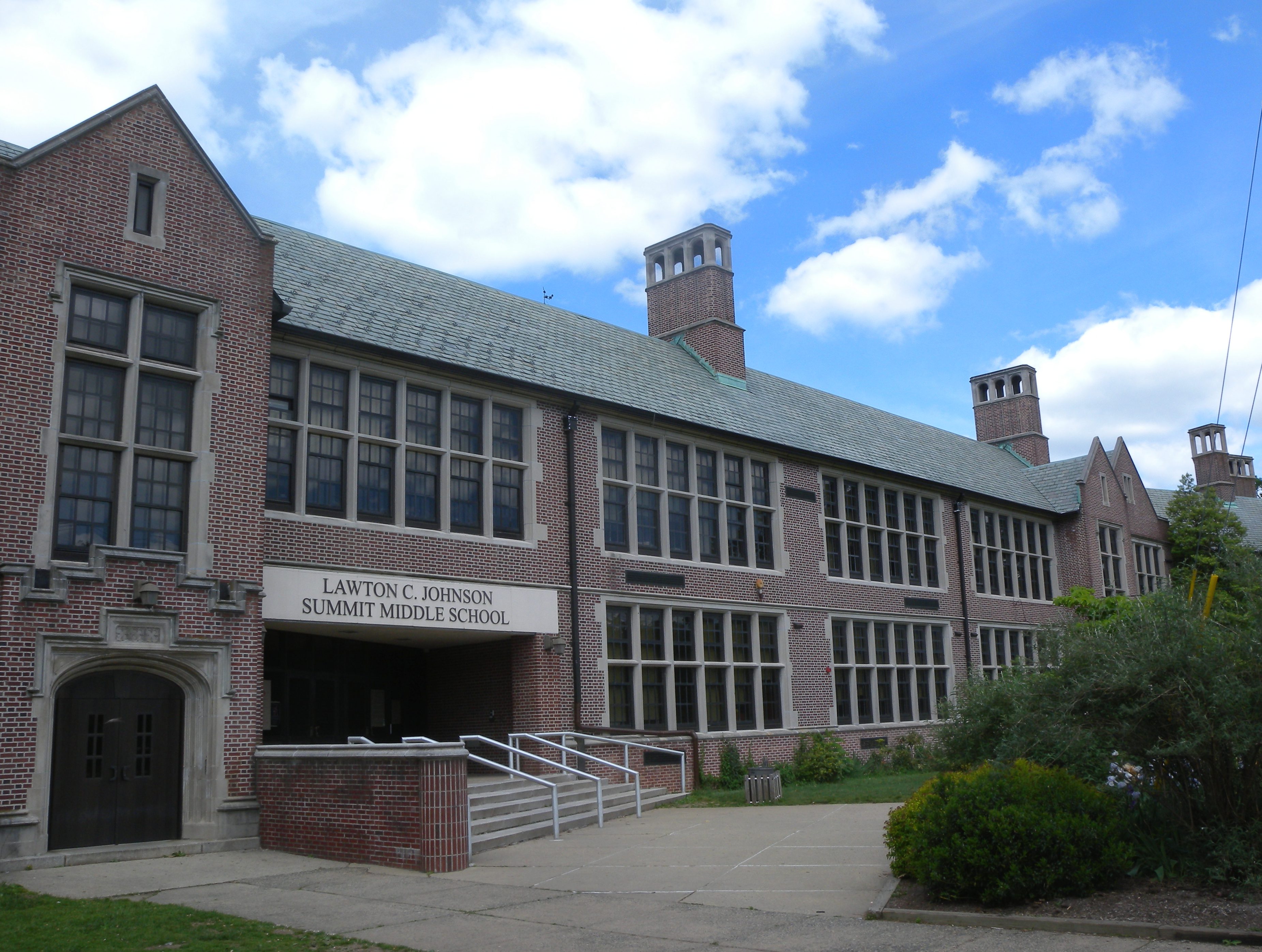 Multi-story brick school building with large windows and a ramp at the entrance, identified by signage.