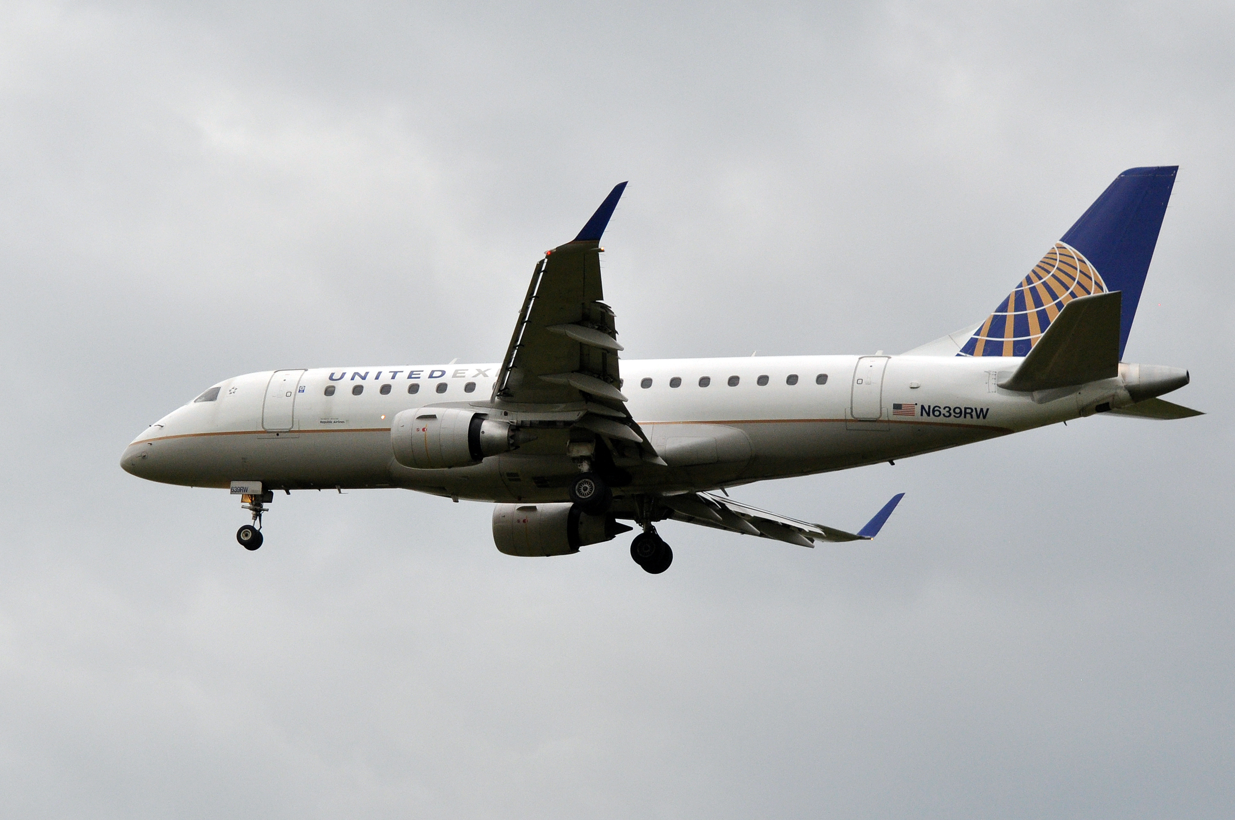 United Airlines regional jet with landing gear deployed against an overcast sky.