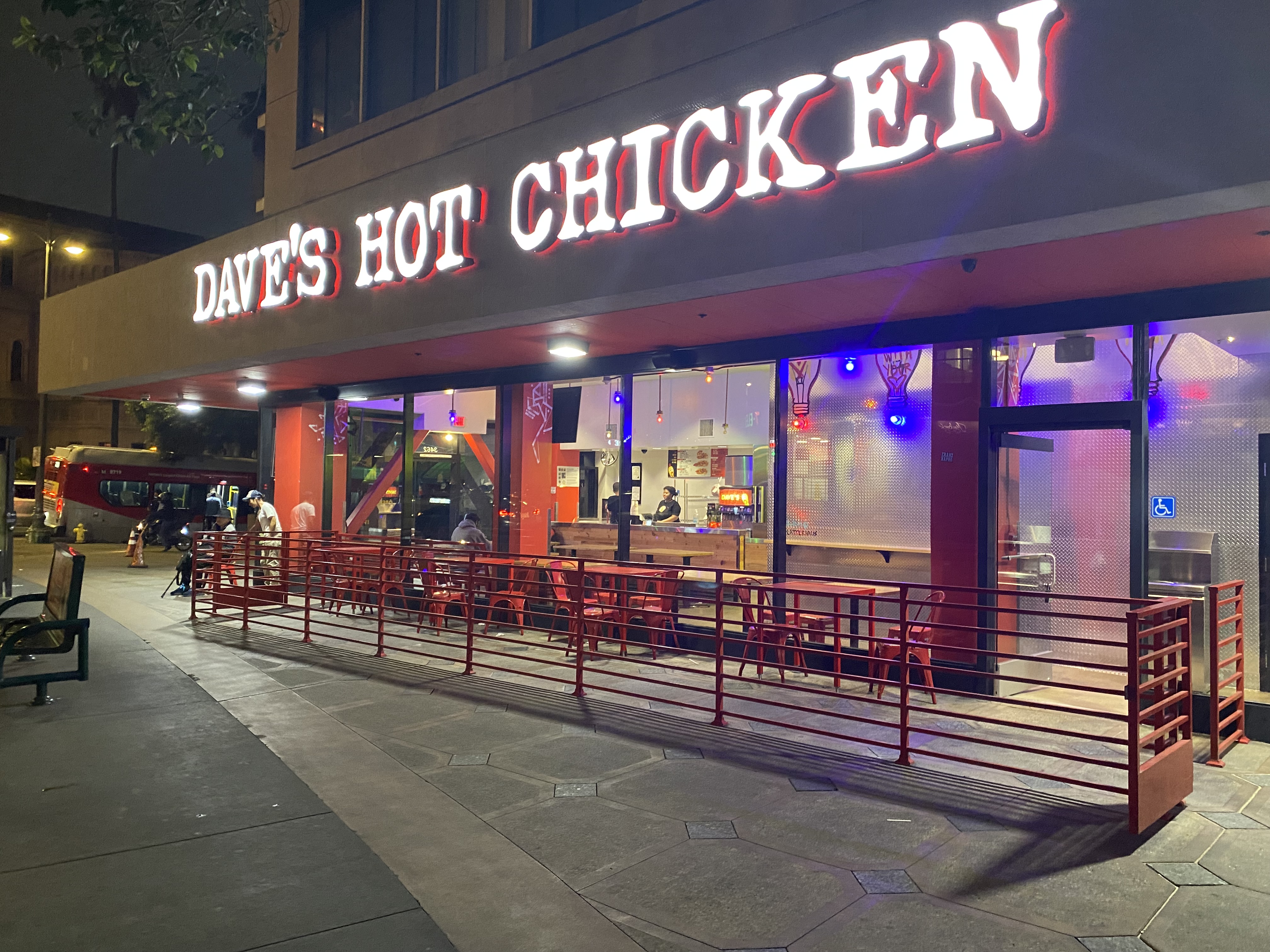 Dave's Hot Chicken restaurant exterior at night with glowing red sign and outdoor seating.