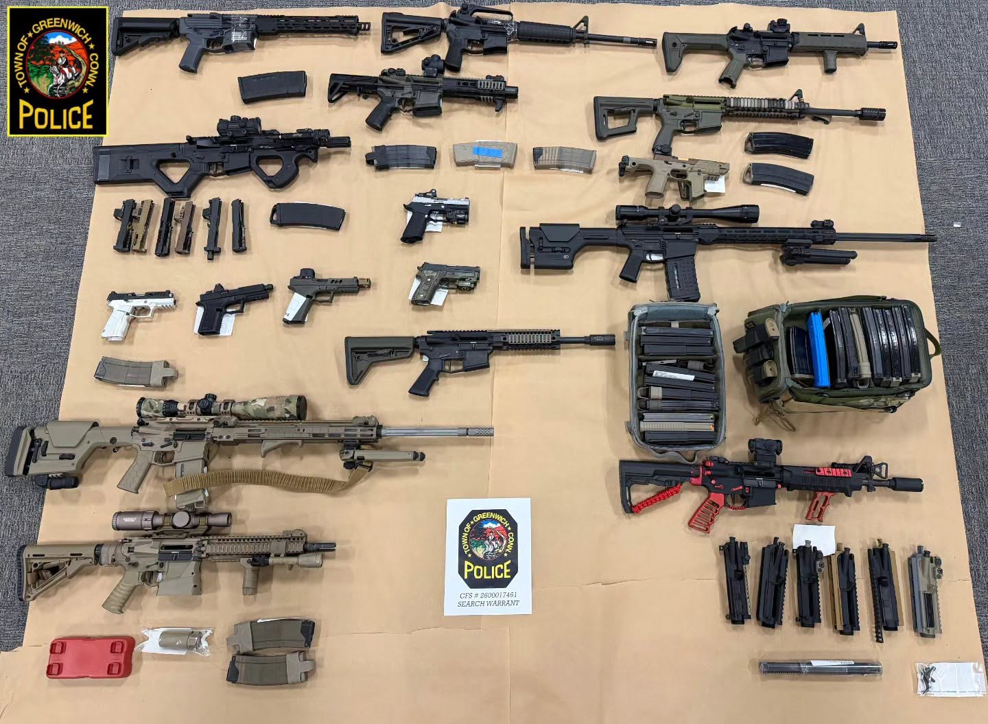 Rows of rifles, handguns, and magazines laid out on a surface beside a police badge.