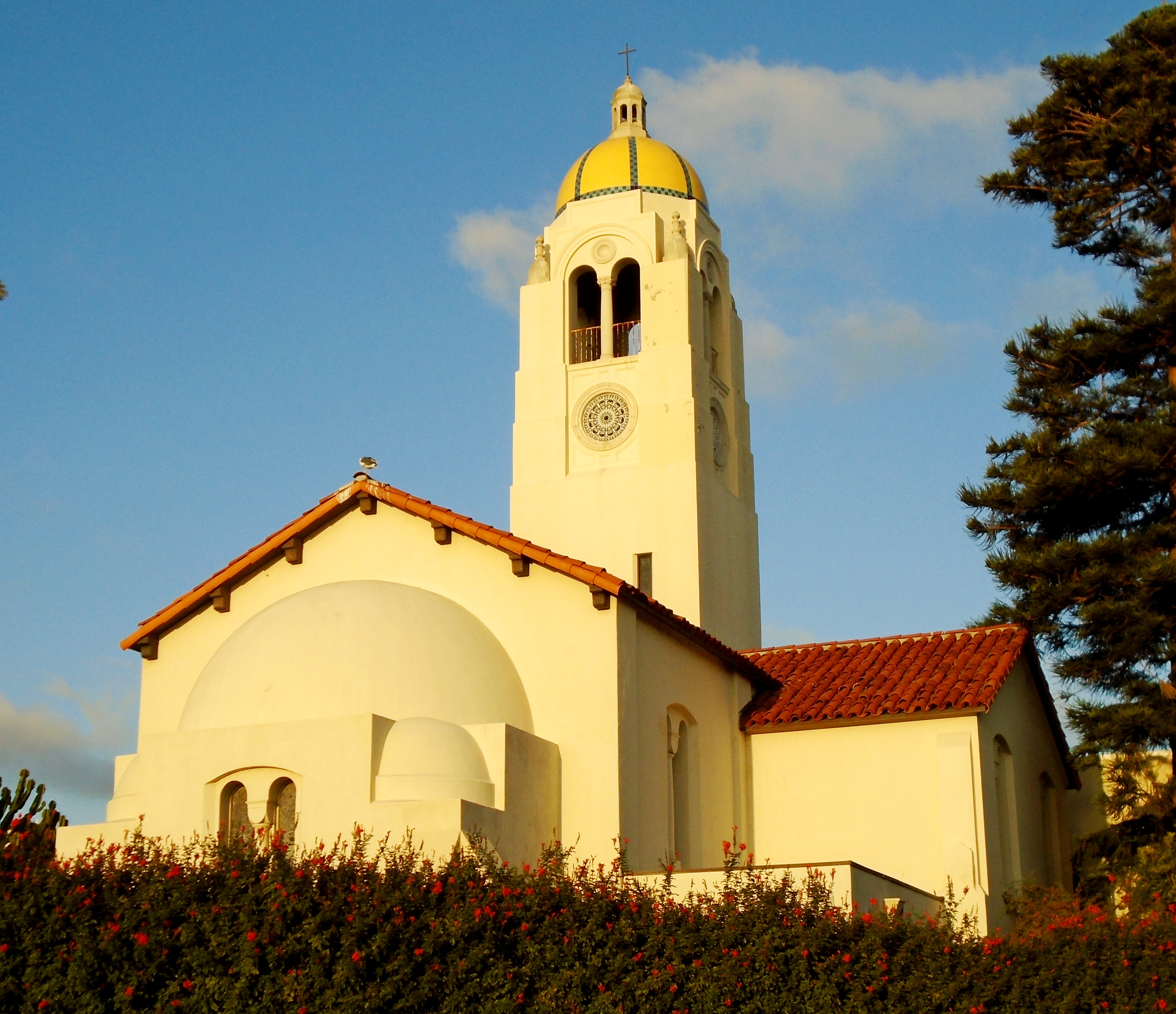 White stucco building with gold dome, bell tower, and red tile roof at dusk.
