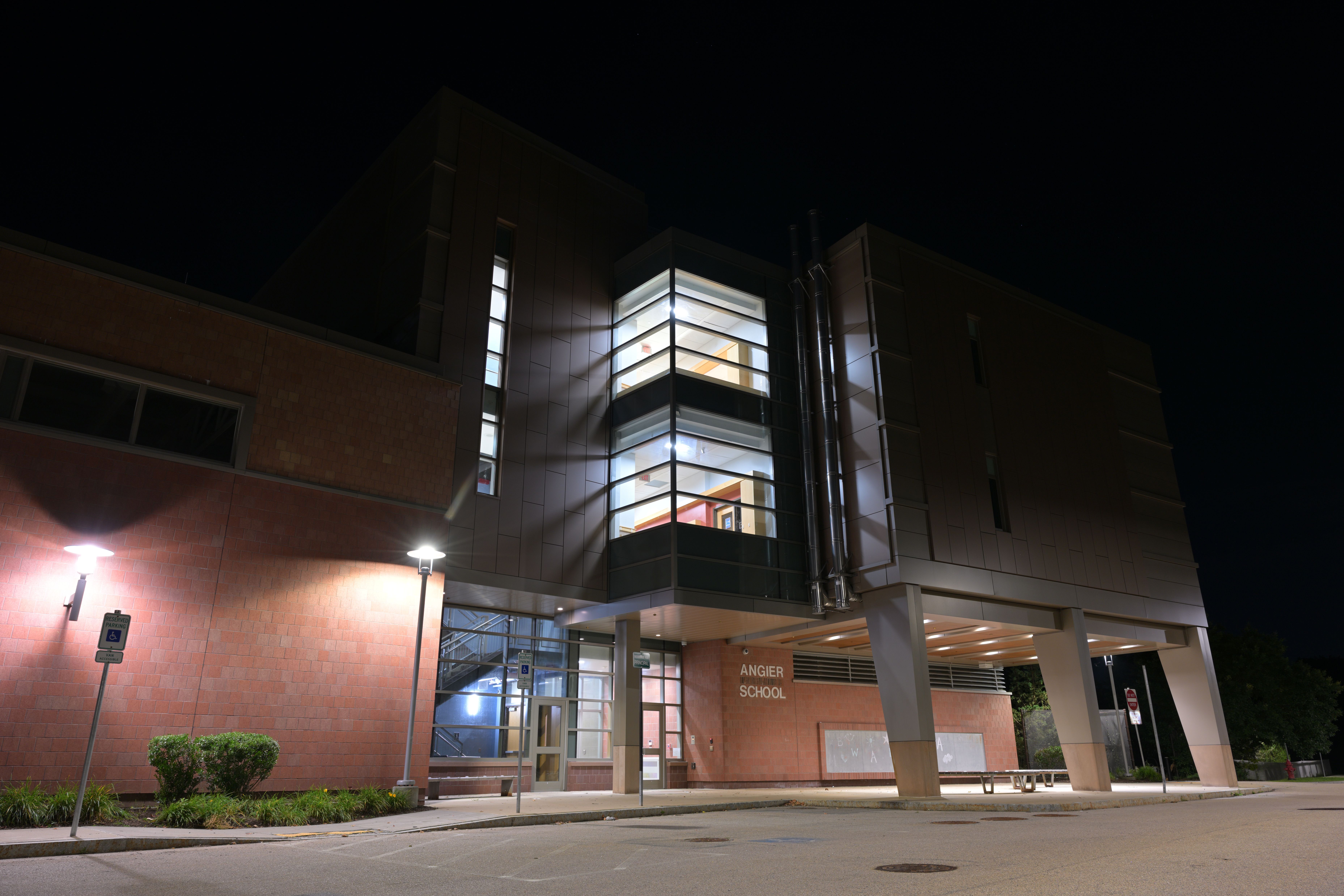 Exterior rear entrance of a multi-story brick and glass school building illuminated at night.