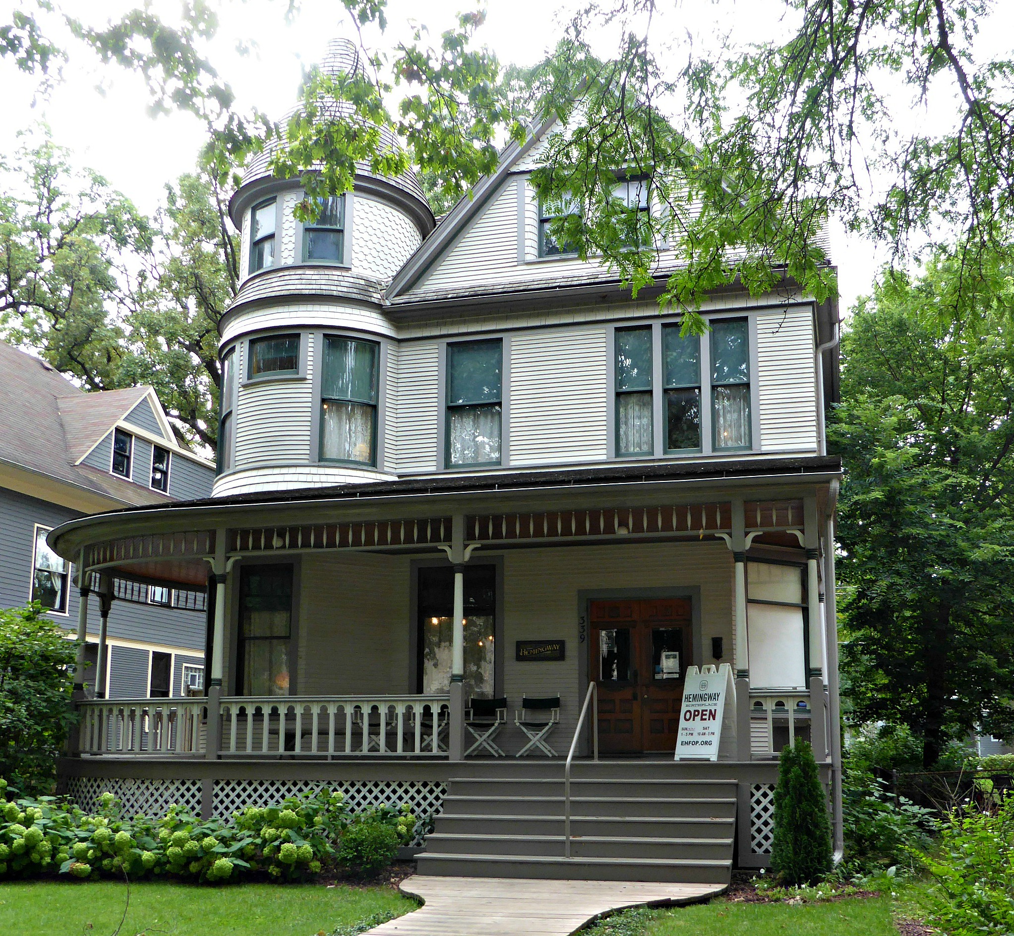 Victorian Queen Anne house with wraparound porch, turret, and surrounding trees.
