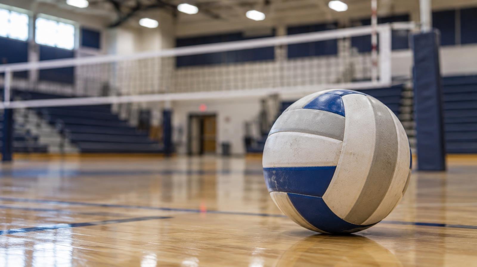 A volleyball resting on a hardwood gymnasium floor near the net.