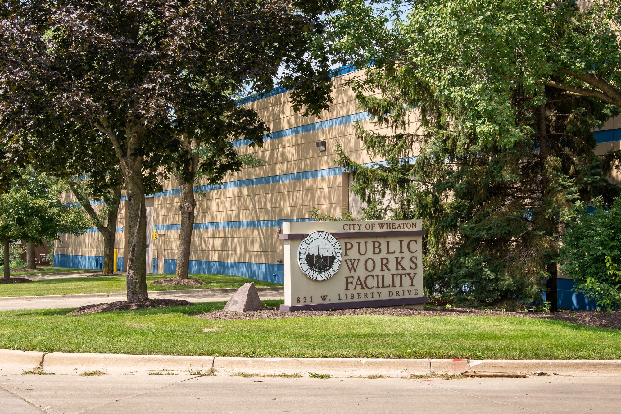 Exterior of a large tan and blue public works building with a monument sign in front.