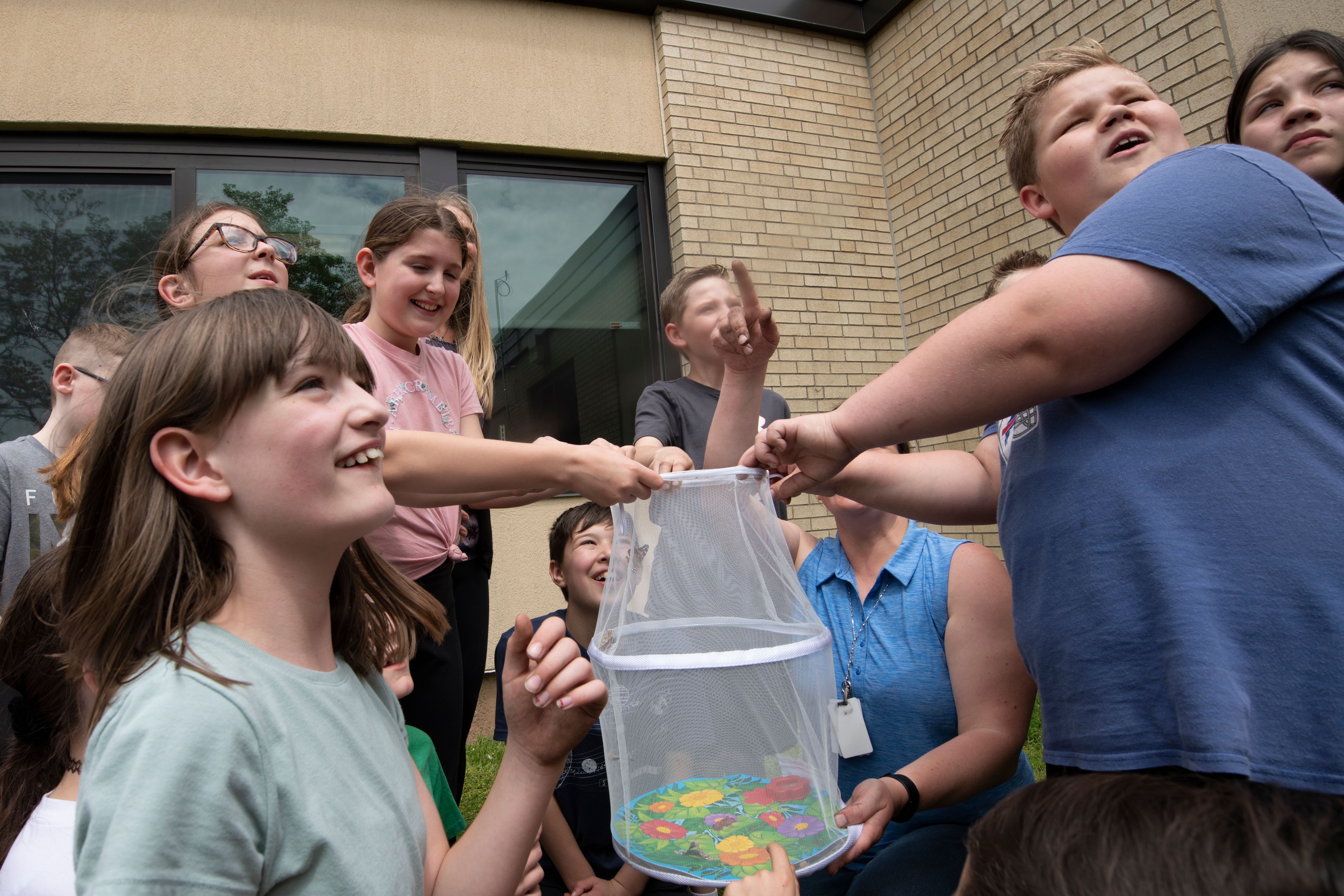A group of children outdoors examining a clear container of materials together.