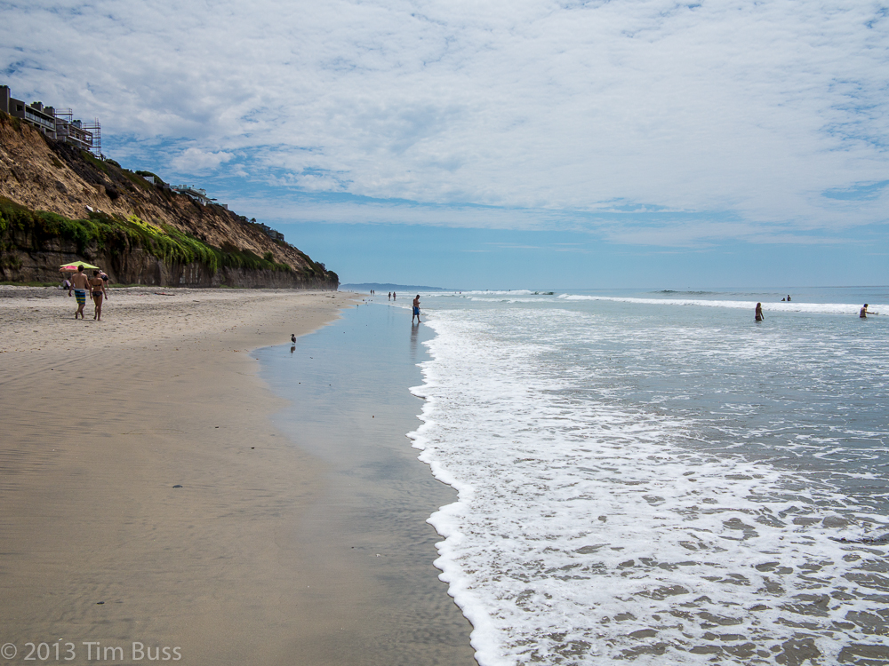 Wide sandy beach with sandstone bluffs and scattered beachgoers along the Encinitas shoreline.