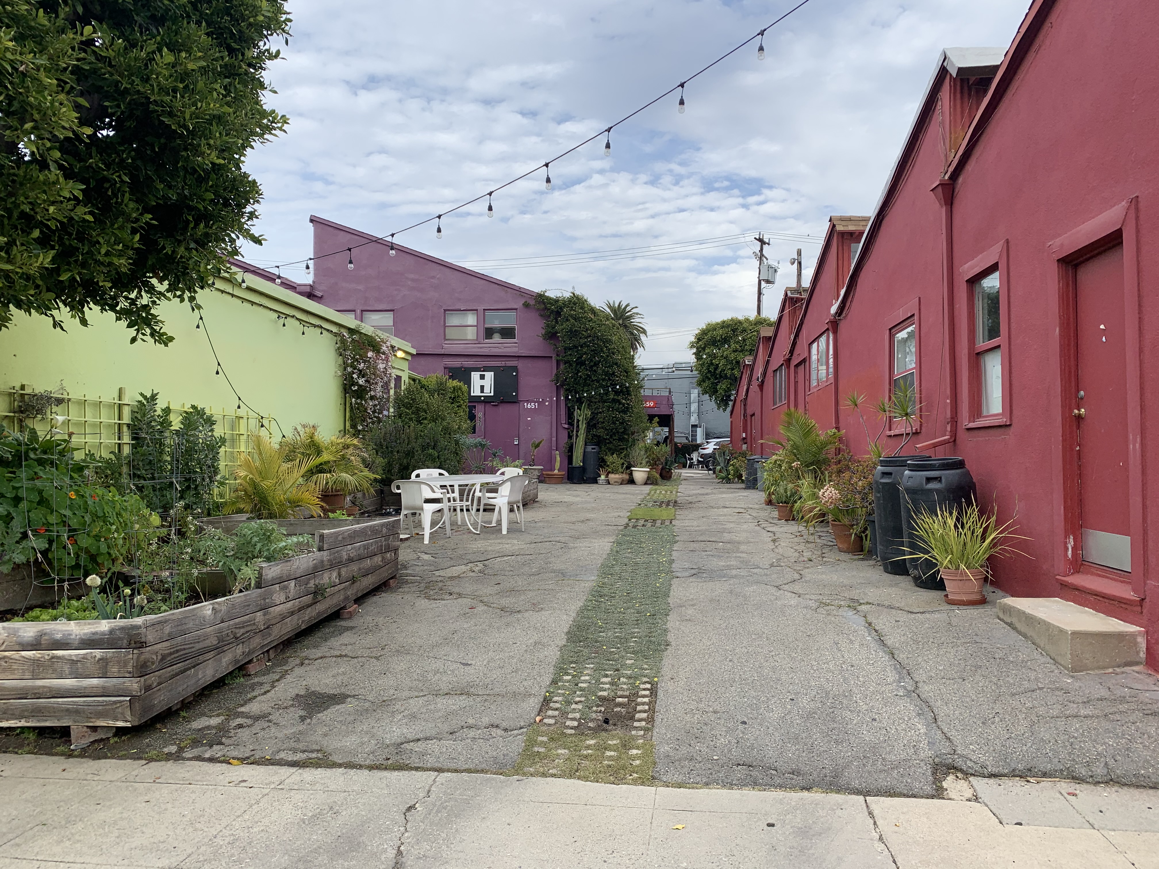 Colorful courtyard with painted walls, string lights, garden beds, and white outdoor furniture between buildings.