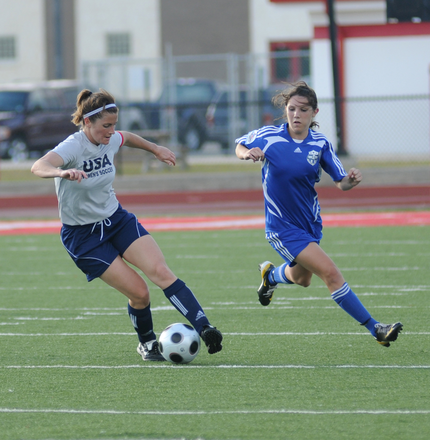 Two female soccer players competing for the ball on a turf field.