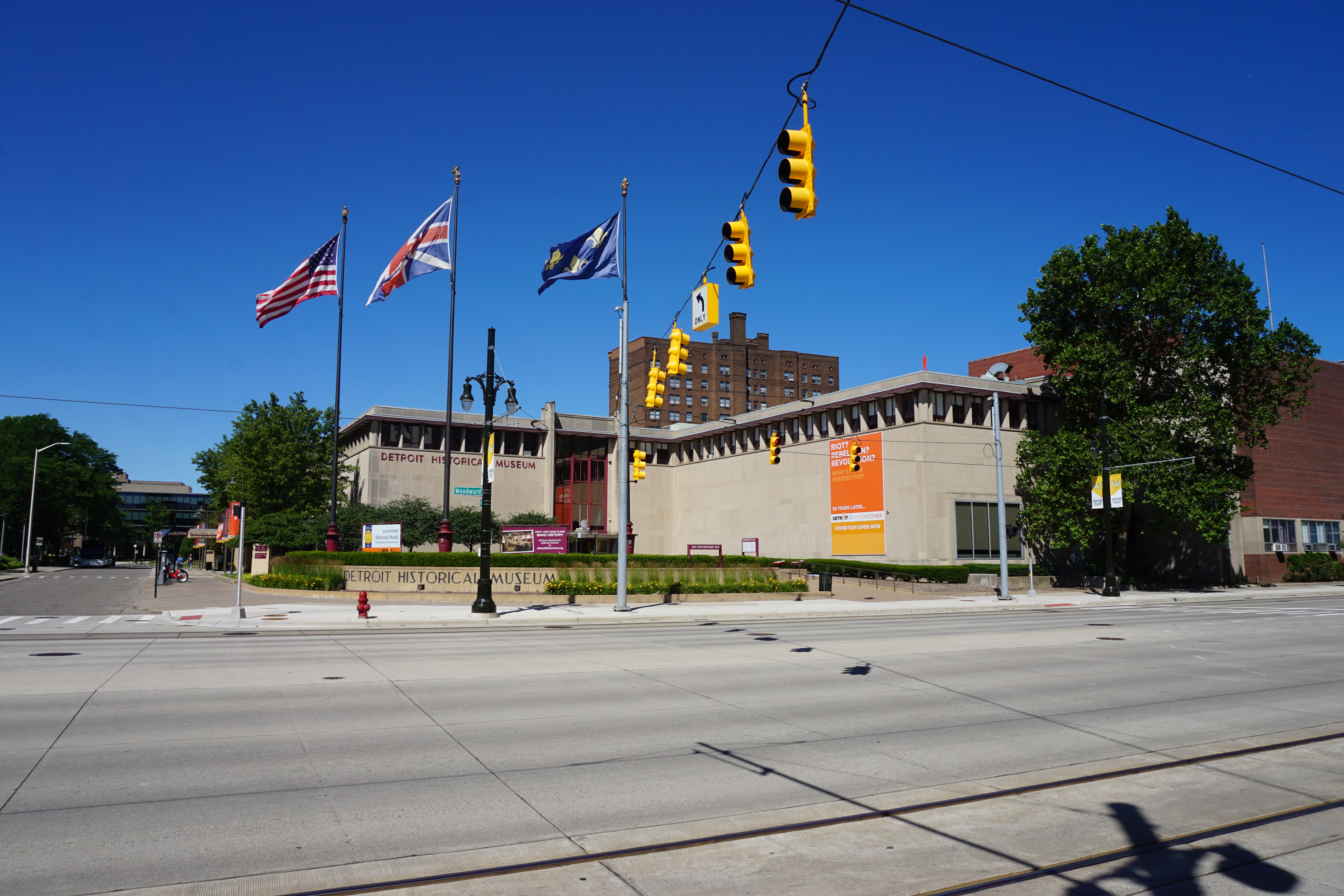 Low-rise stone museum building with flags on poles in front under a clear blue sky