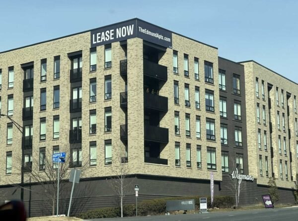 Multi-story brick apartment building with a 'Lease Now' banner above a Wegmans storefront.