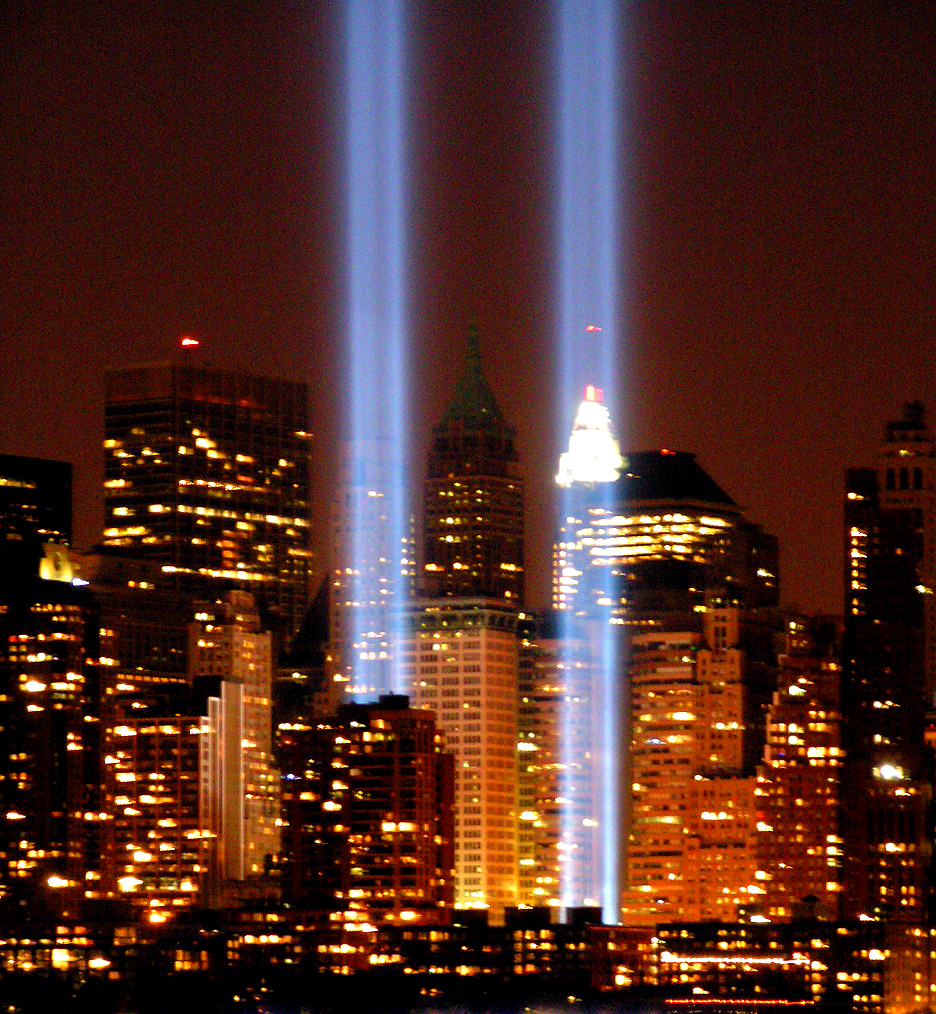 Two tall beams of light rise from the Manhattan skyline at dusk.