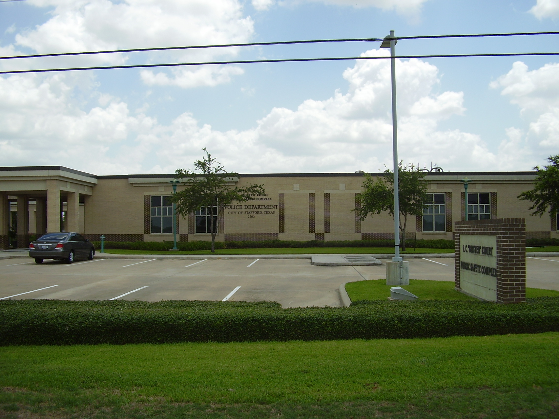Single-story tan brick police building with a parking lot and brick sign out front.