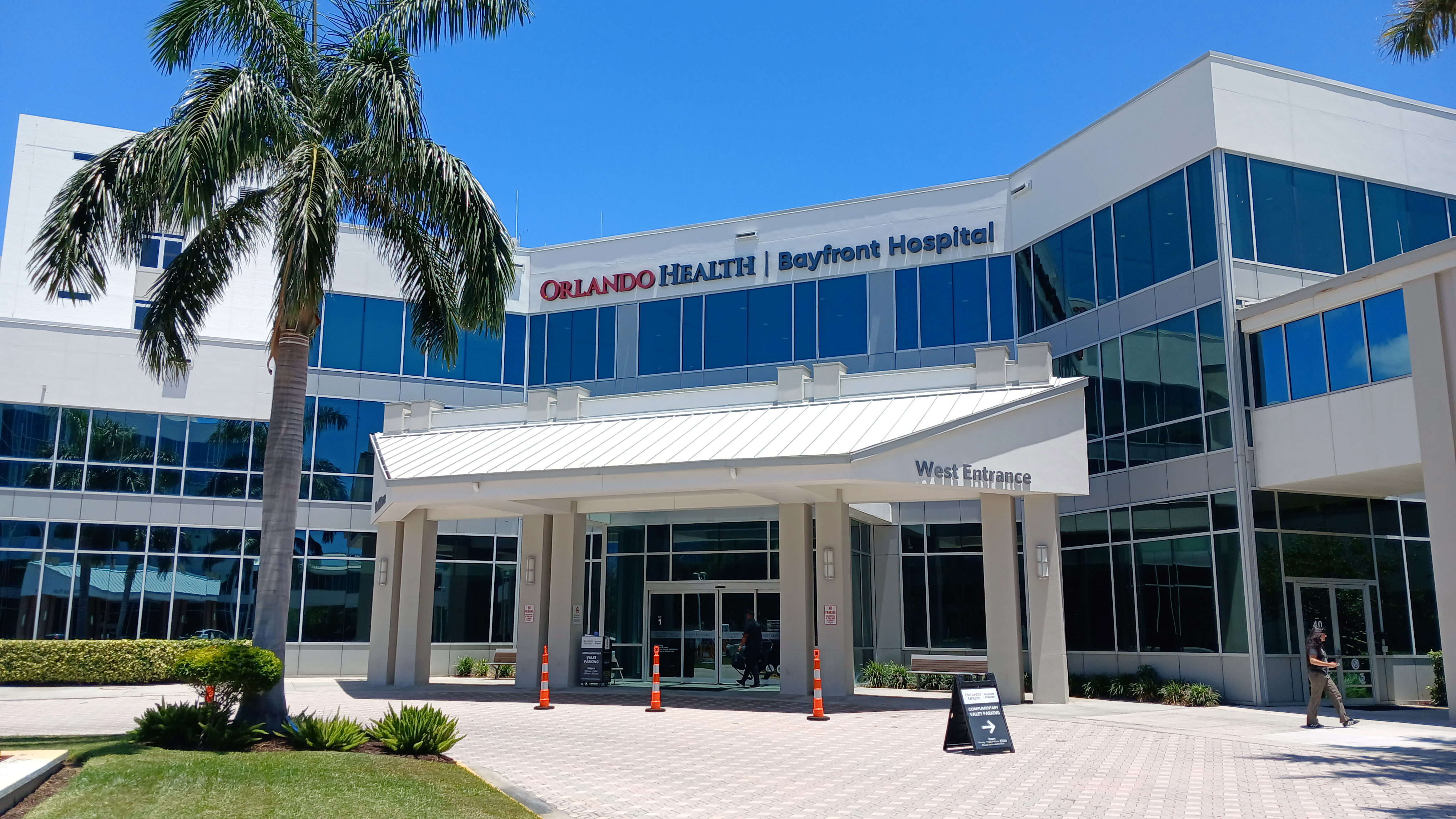 Exterior entrance of an Orlando Health hospital with blue glass windows and palm trees.