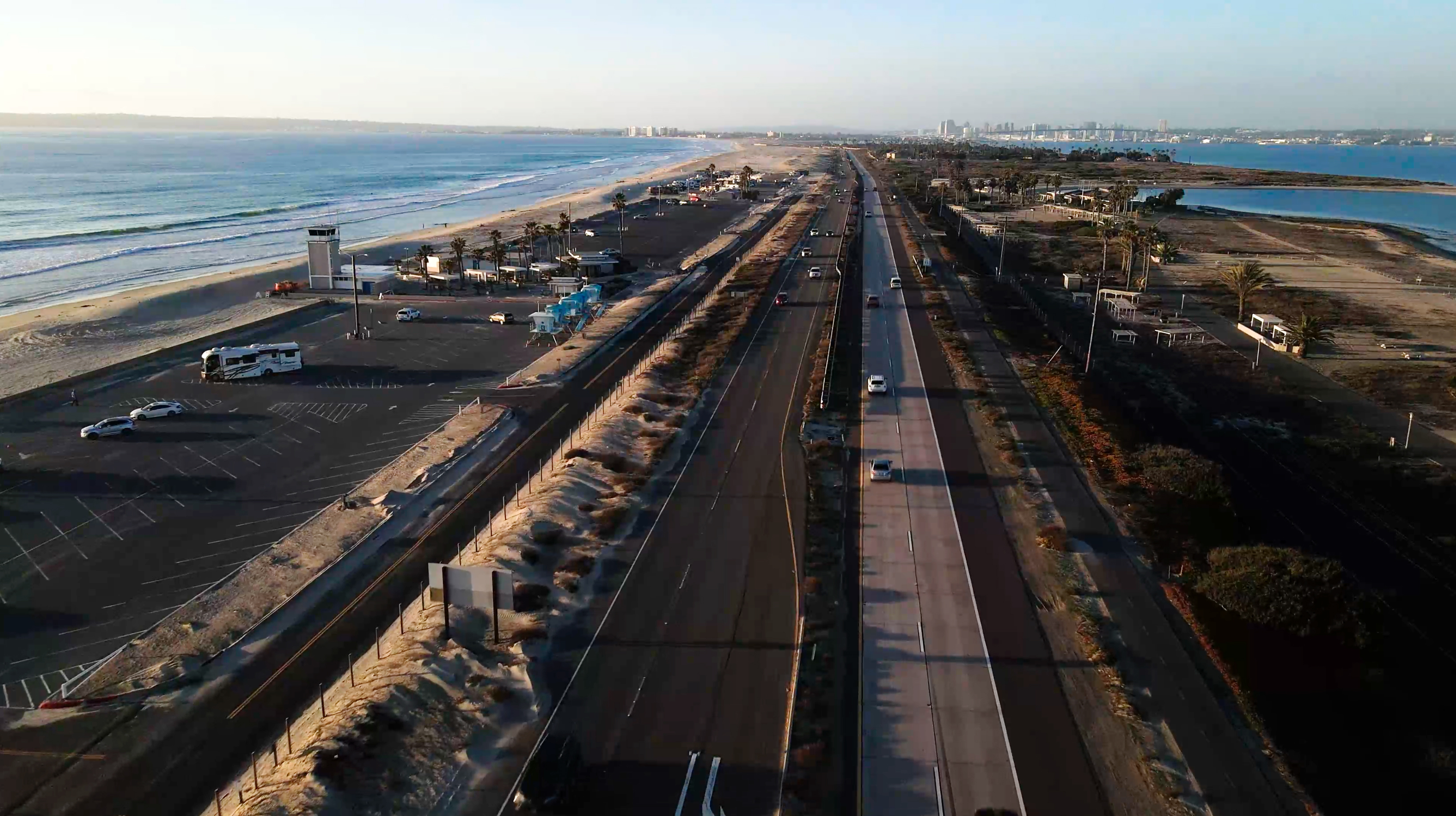 Aerial view of a narrow coastal strip with a highway between the ocean and a bay.