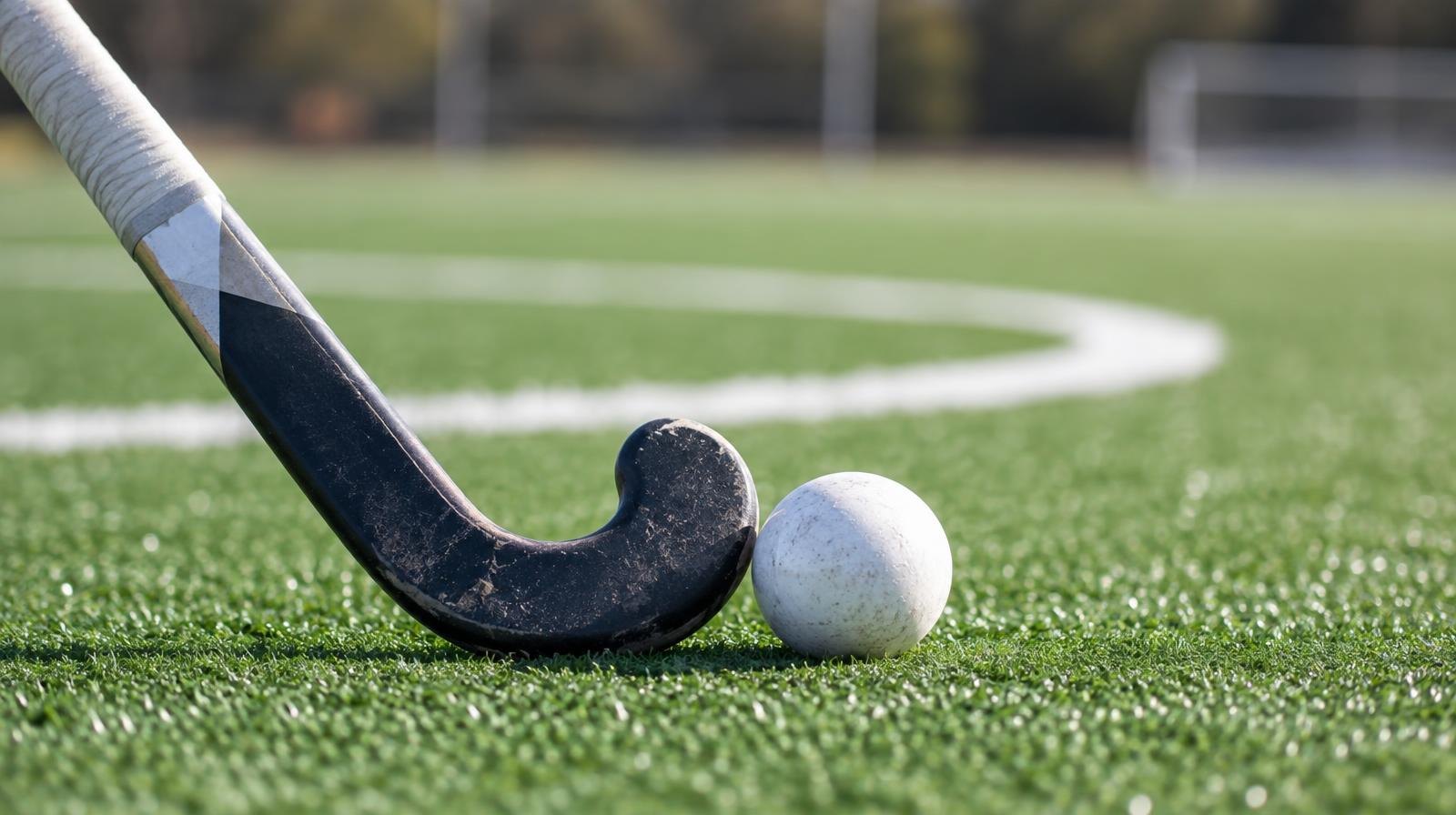 A field hockey stick and ball resting on green artificial turf near a white painted circle.