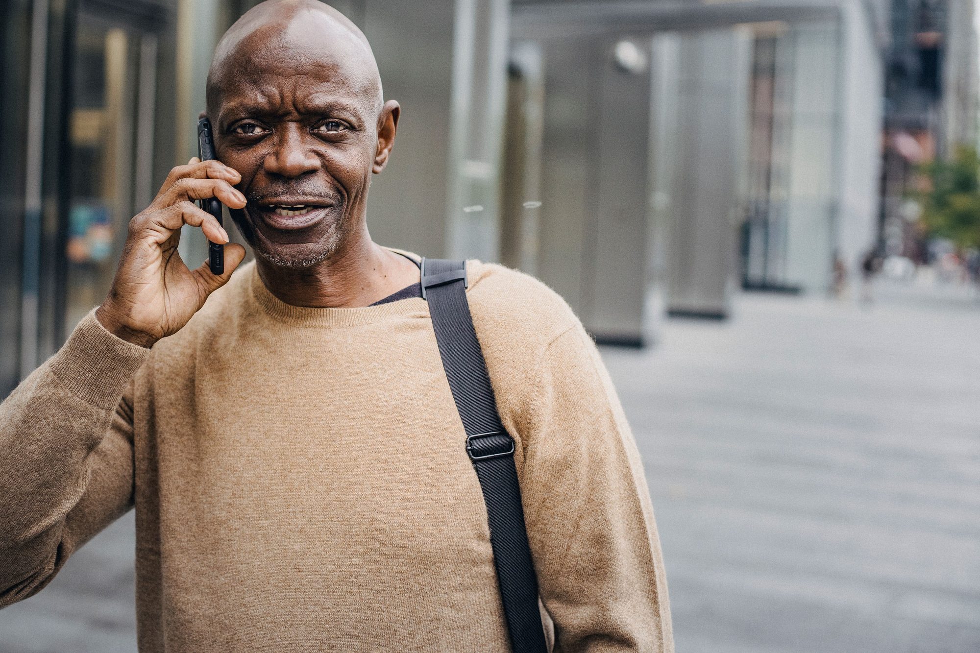 Middle aged African American male entrepreneur in casual clothes walking on city street and having phone conversation in daytime