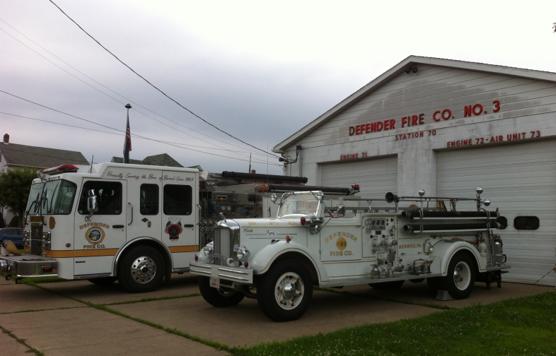 Two fire engines parked outside a small white volunteer fire station building.