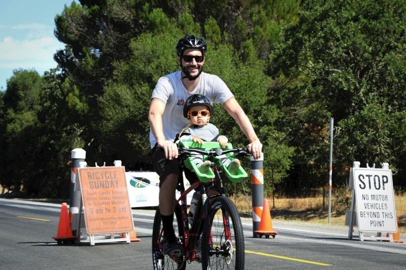 Adult and child in helmets ride a bicycle on a road closed to motor vehicles.