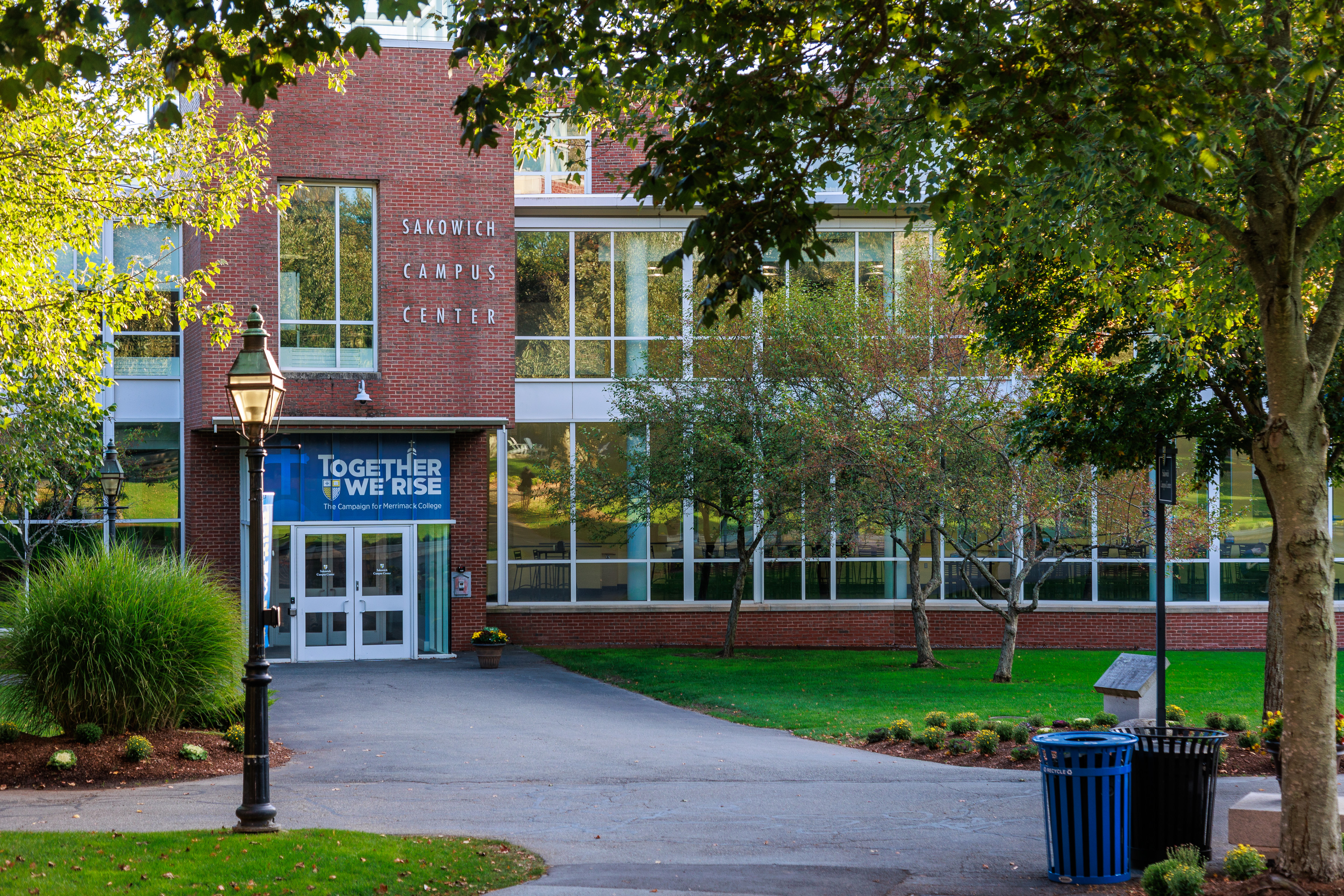 Brick and glass campus center building with a banner at the entrance, surrounded by trees.