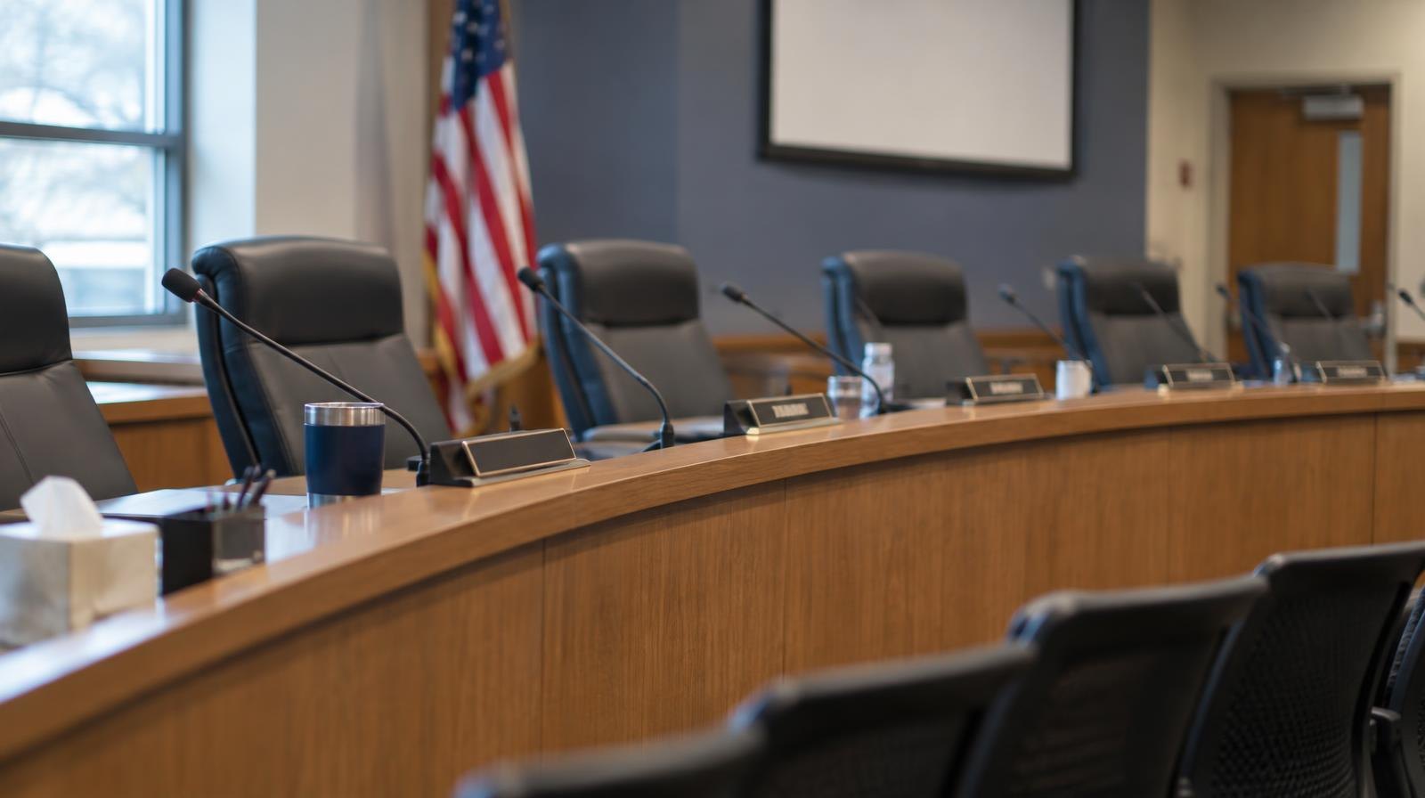 Empty curved dais with microphones and name placards in a meeting room.