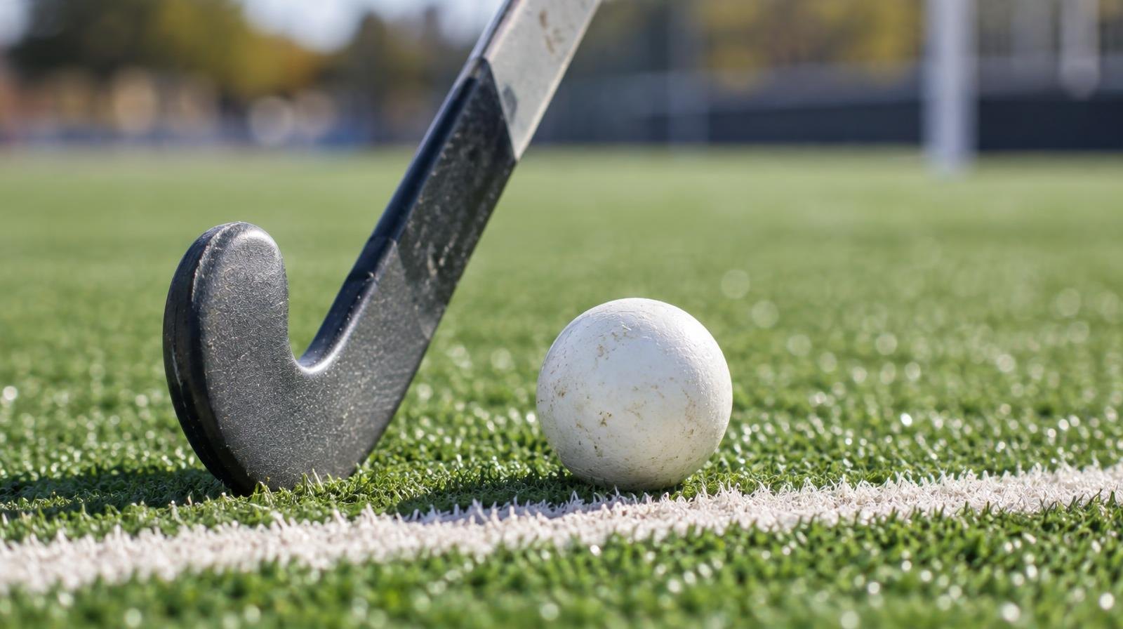 A field hockey stick and ball resting on green artificial turf near a white line.