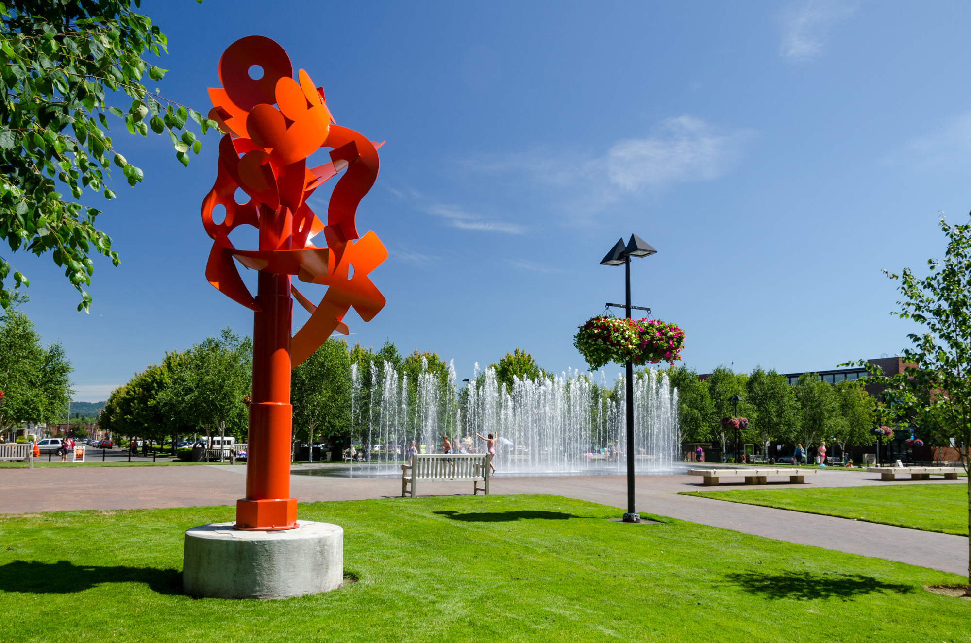 Large orange abstract metal sculpture in a grassy park on a sunny day.