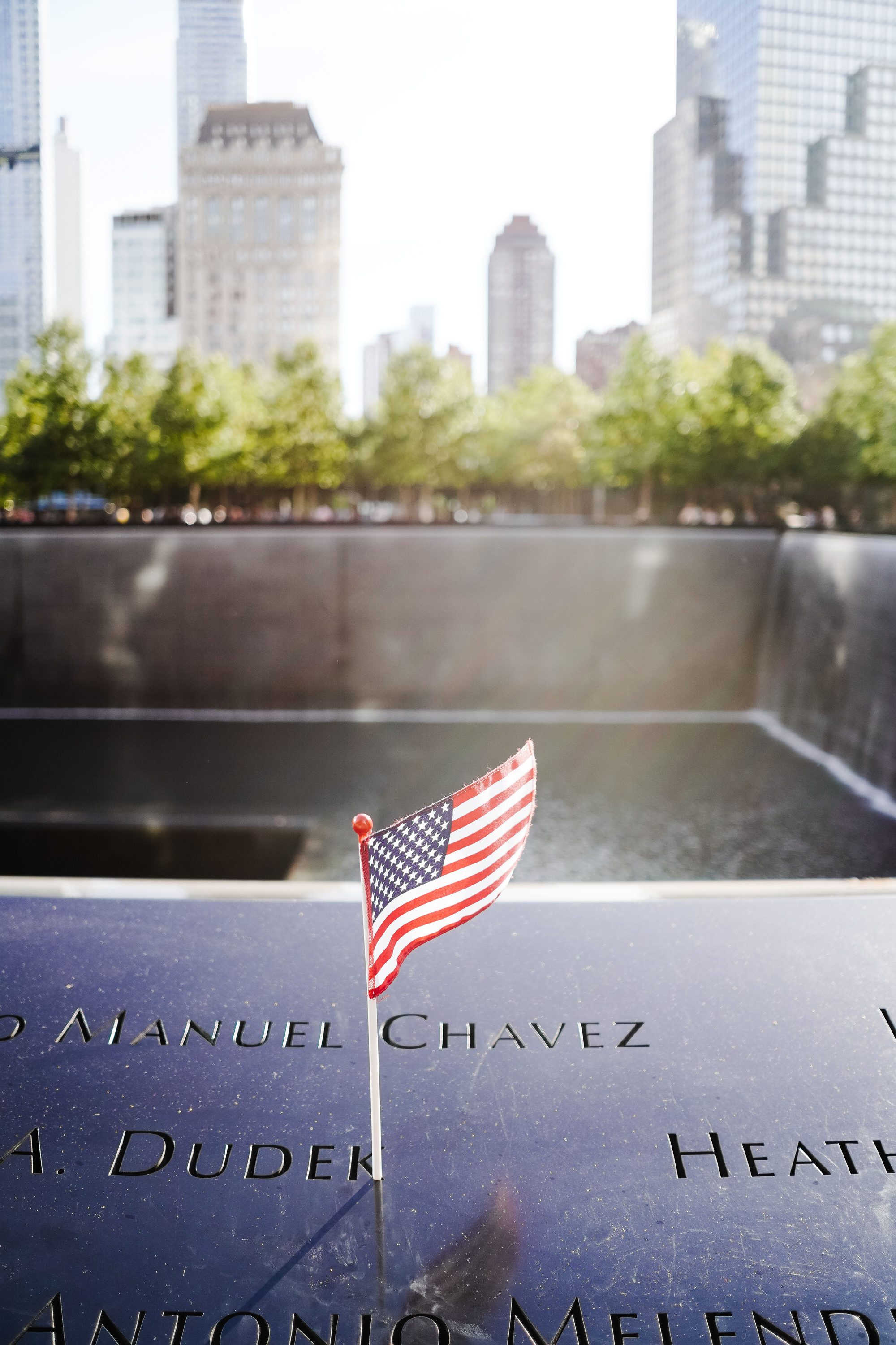 A small American flag at the 9/11 Memorial in New York City with cityscape backdrop.