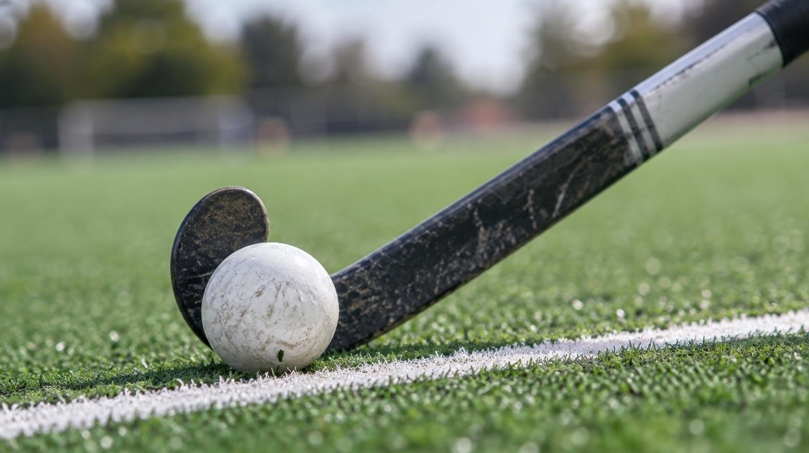 A field hockey stick and ball resting on green artificial turf near a white line.