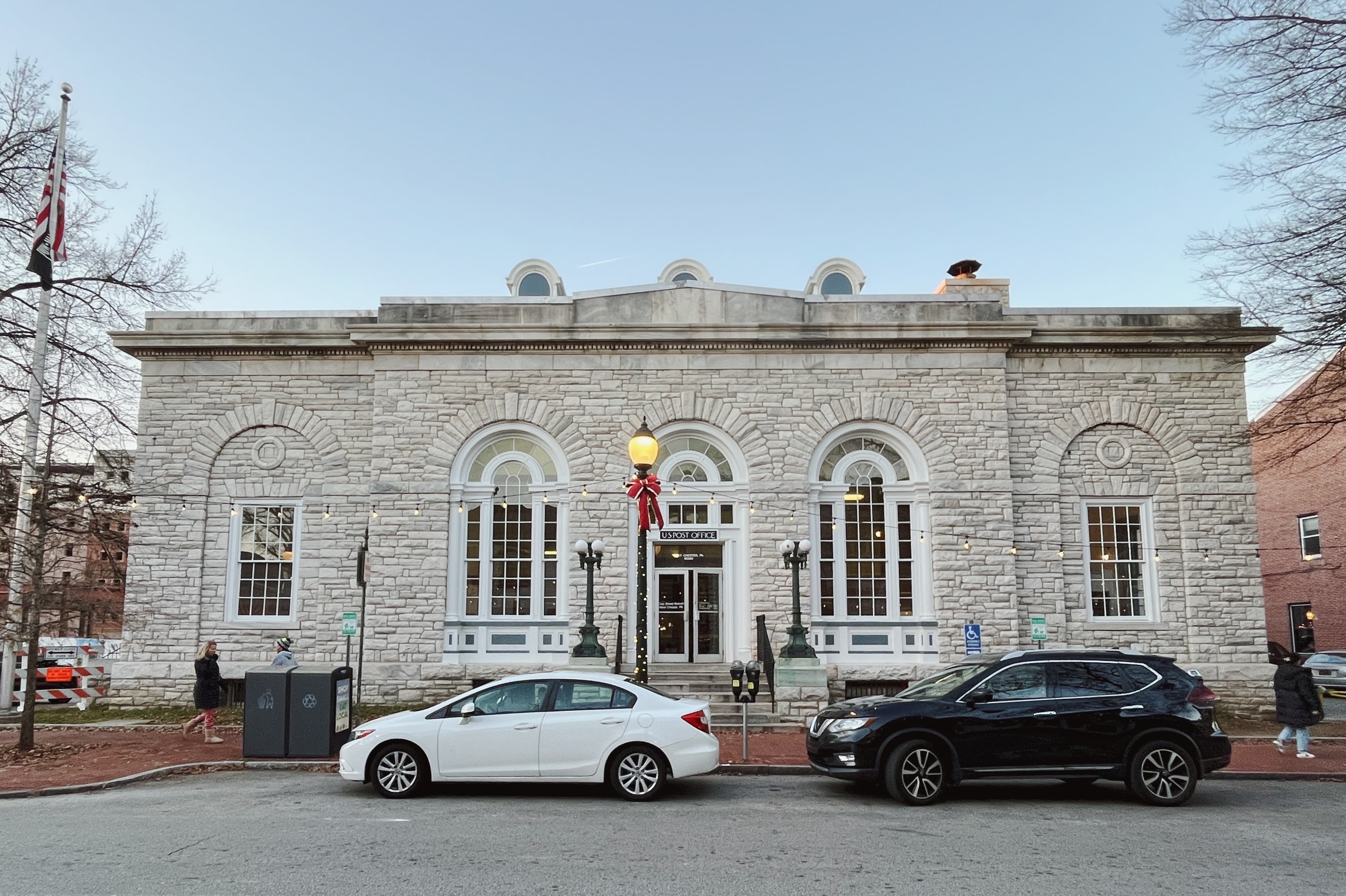 Neoclassical stone building with arched windows and an American flag on a winter day.