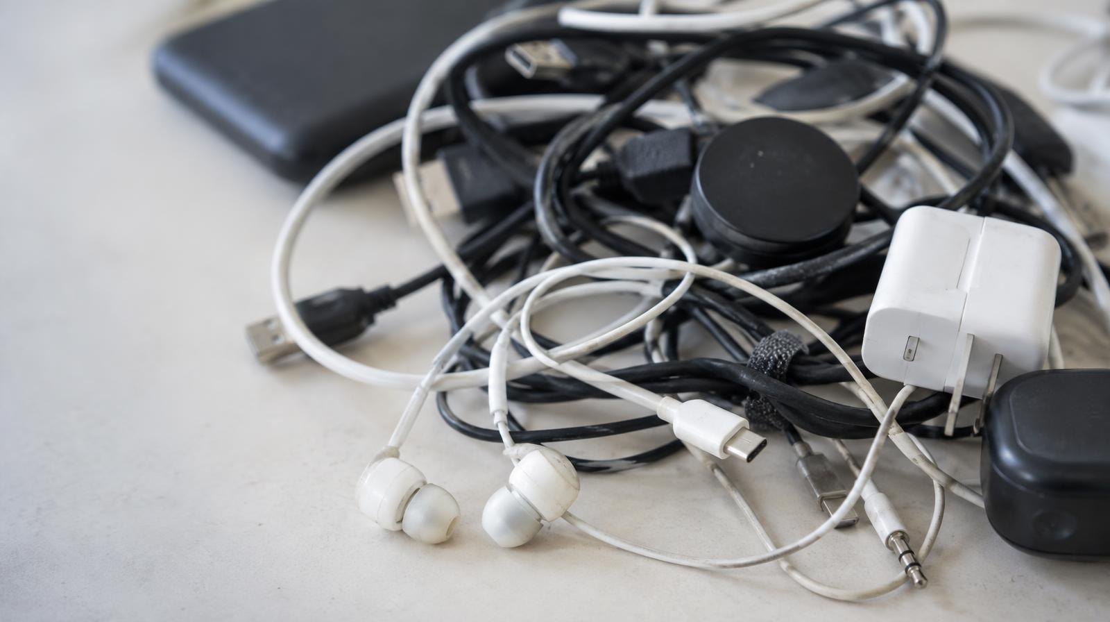 Tangled pile of old earbuds and USB charging cables on a light surface.