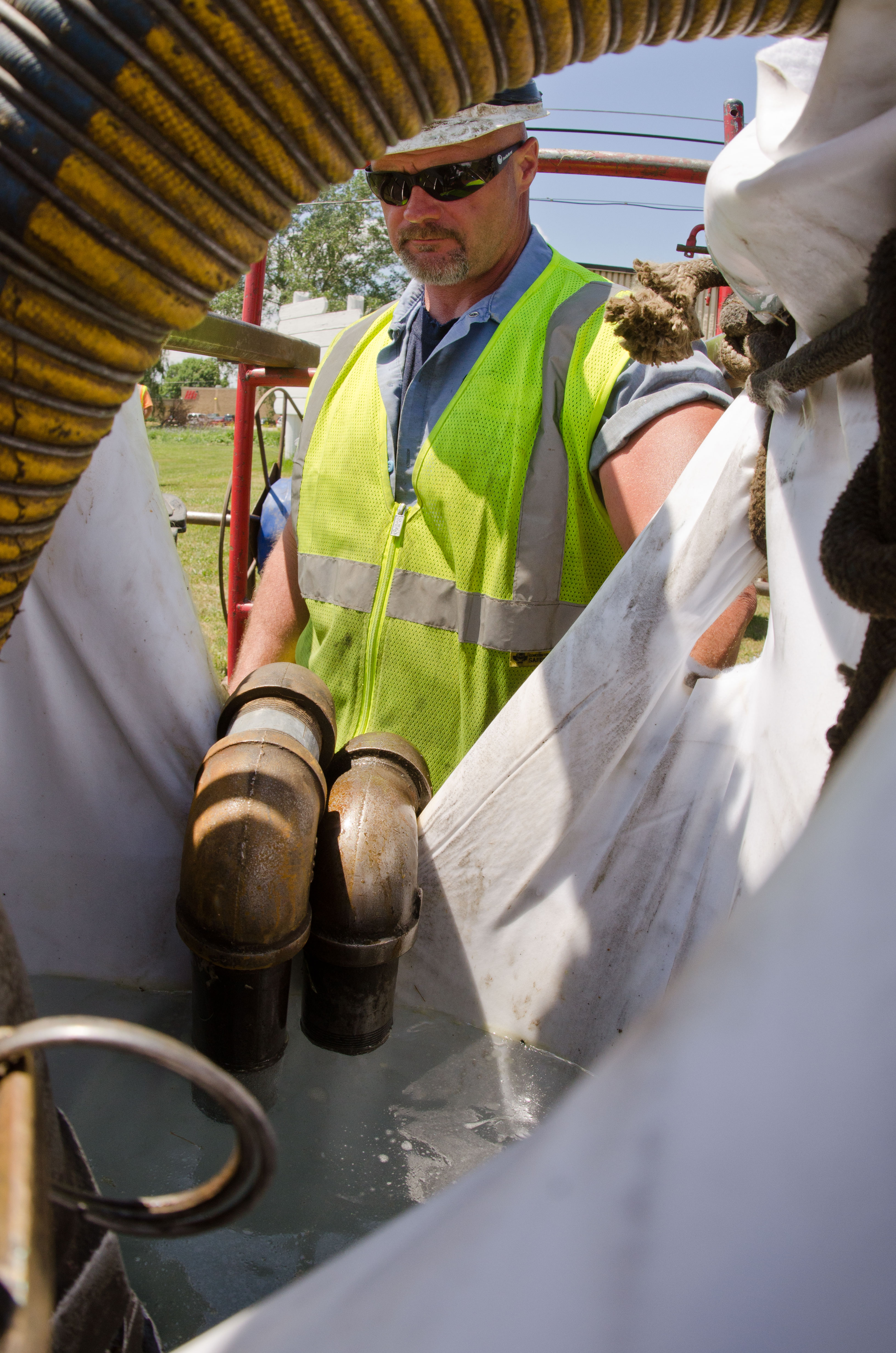Worker in safety vest overseeing a white pipe liner being fed into a sewer manhole.
