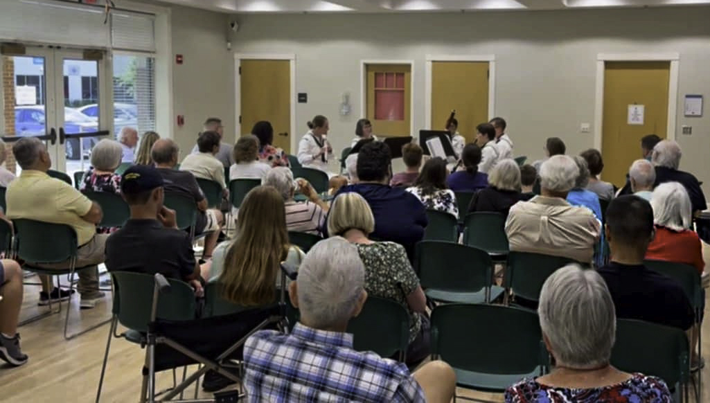 Audience seated in rows of green chairs in a library meeting room.