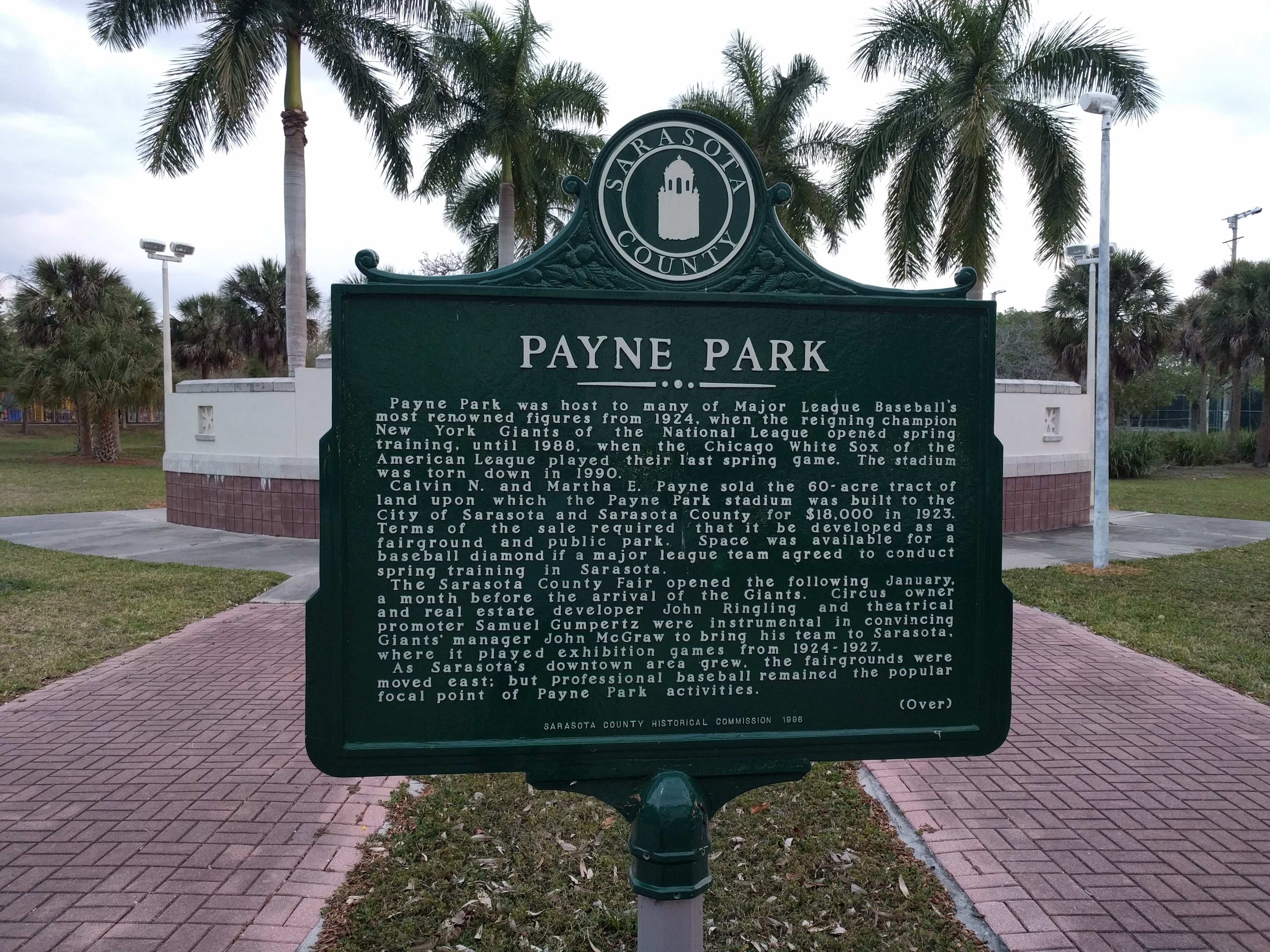 Green historical marker sign for Payne Park on a post, palm trees visible behind it.